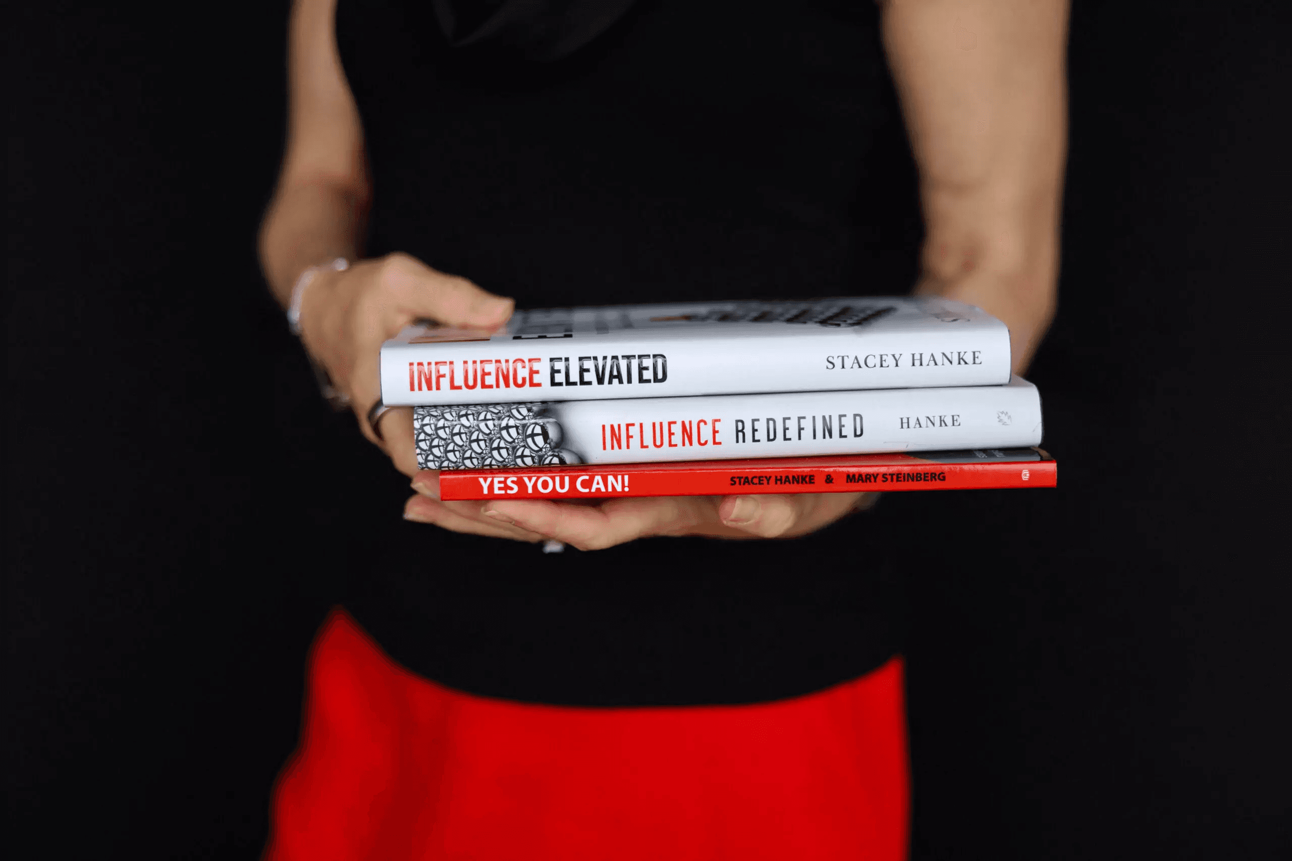 Woman holding books "Influence Elevated", "Influence Redefined", and "Yes You Can"