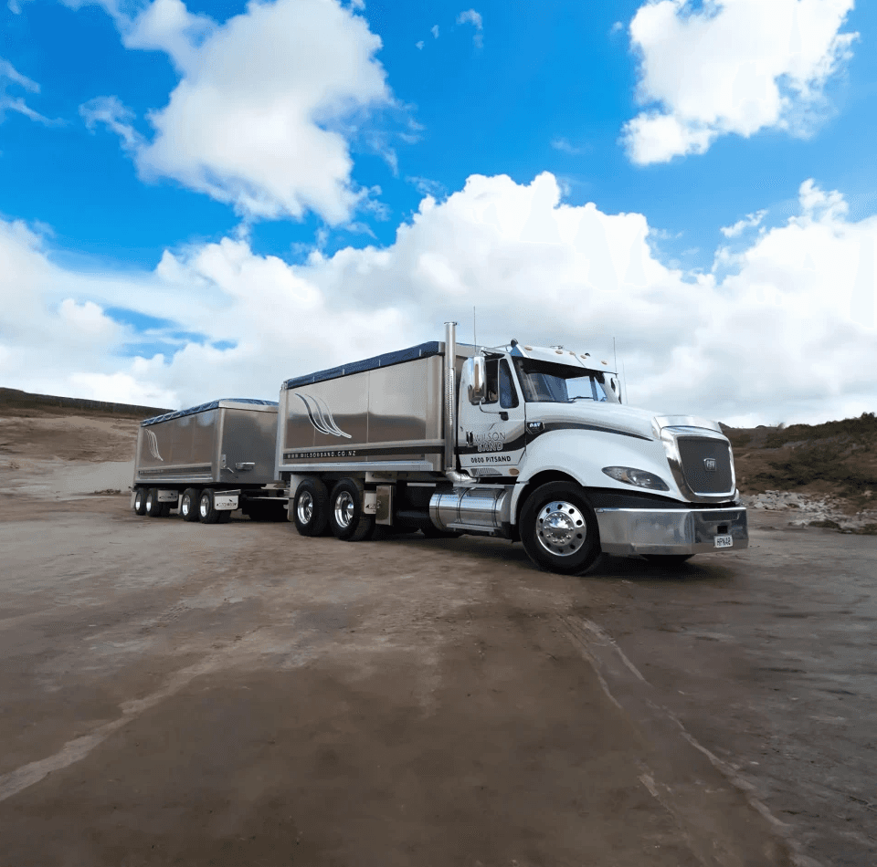 A large semi-truck and trailer parked in a sand quarry