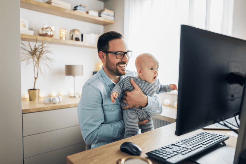 a man holding a baby and looking at a computer screen