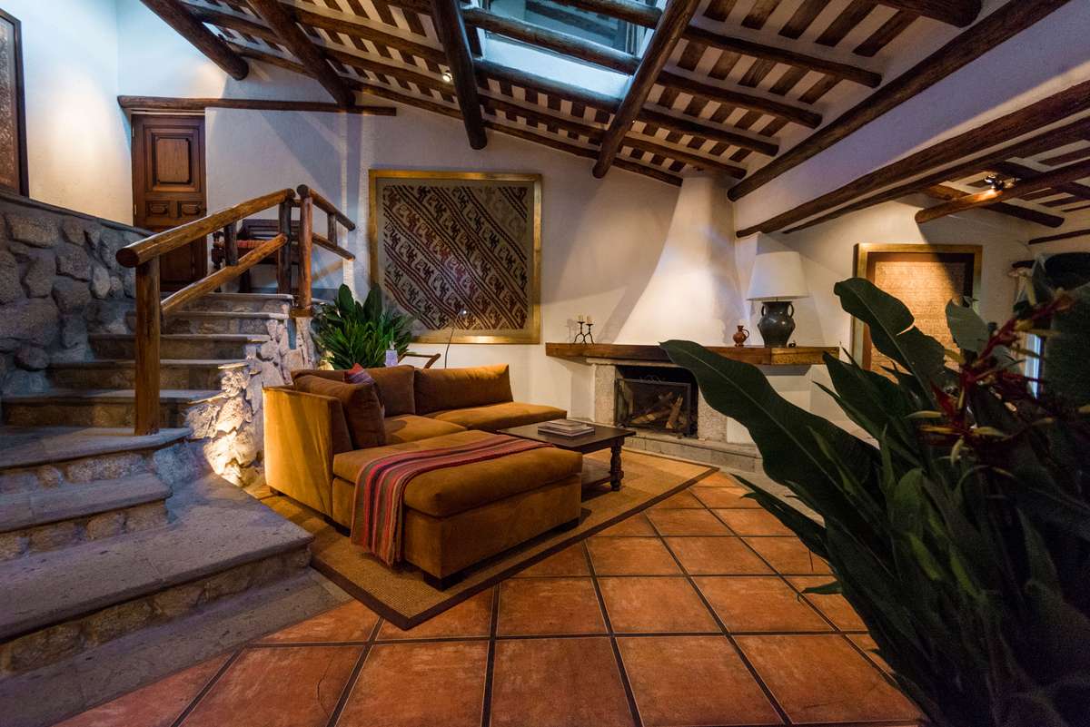 A rustic lounge with a leather sofa and armchair under a beamed ceiling with a skylight over terracotta tile flooring.