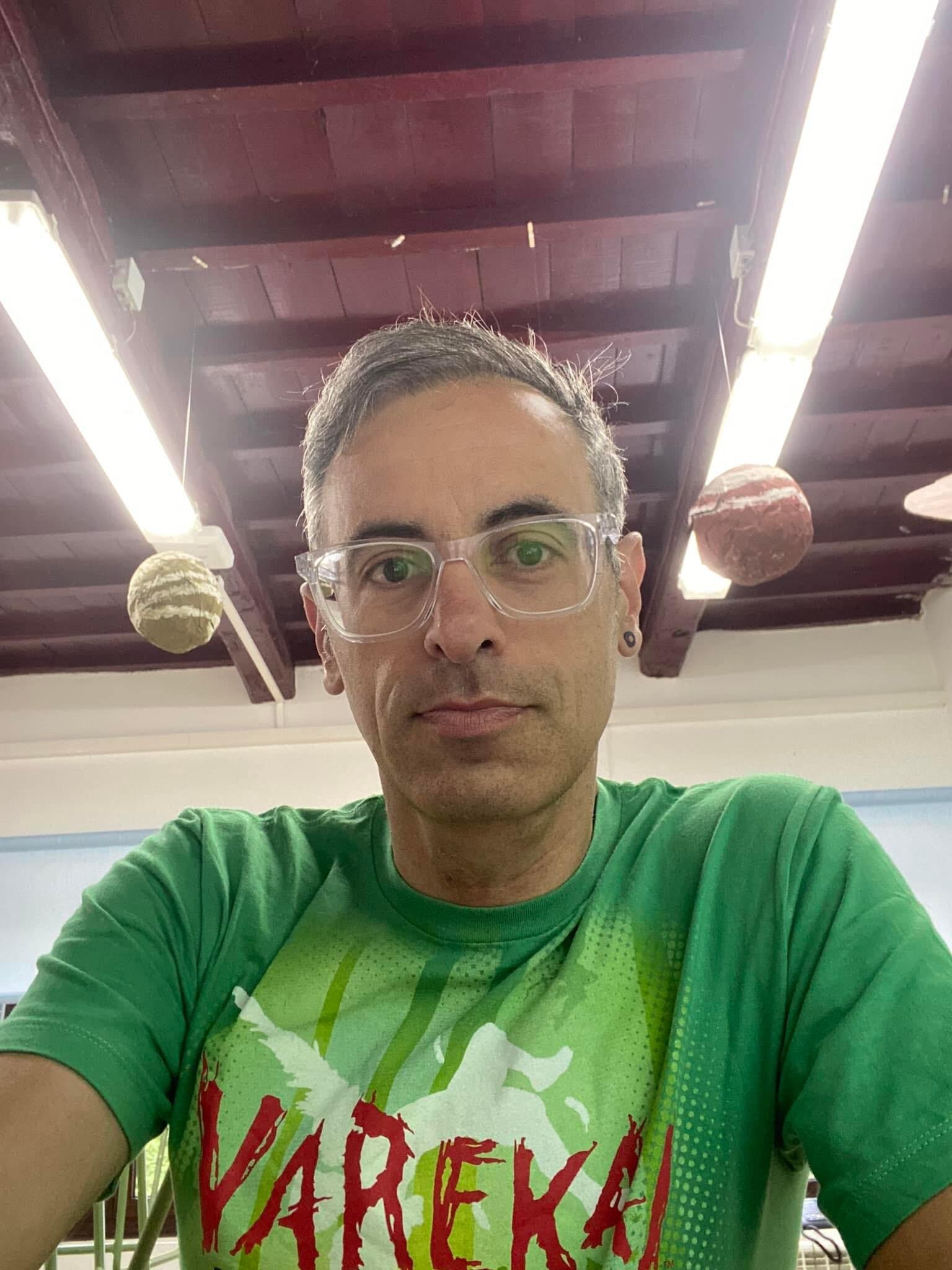 Man wearing glasses and a green shirt inside a brightly lit room.