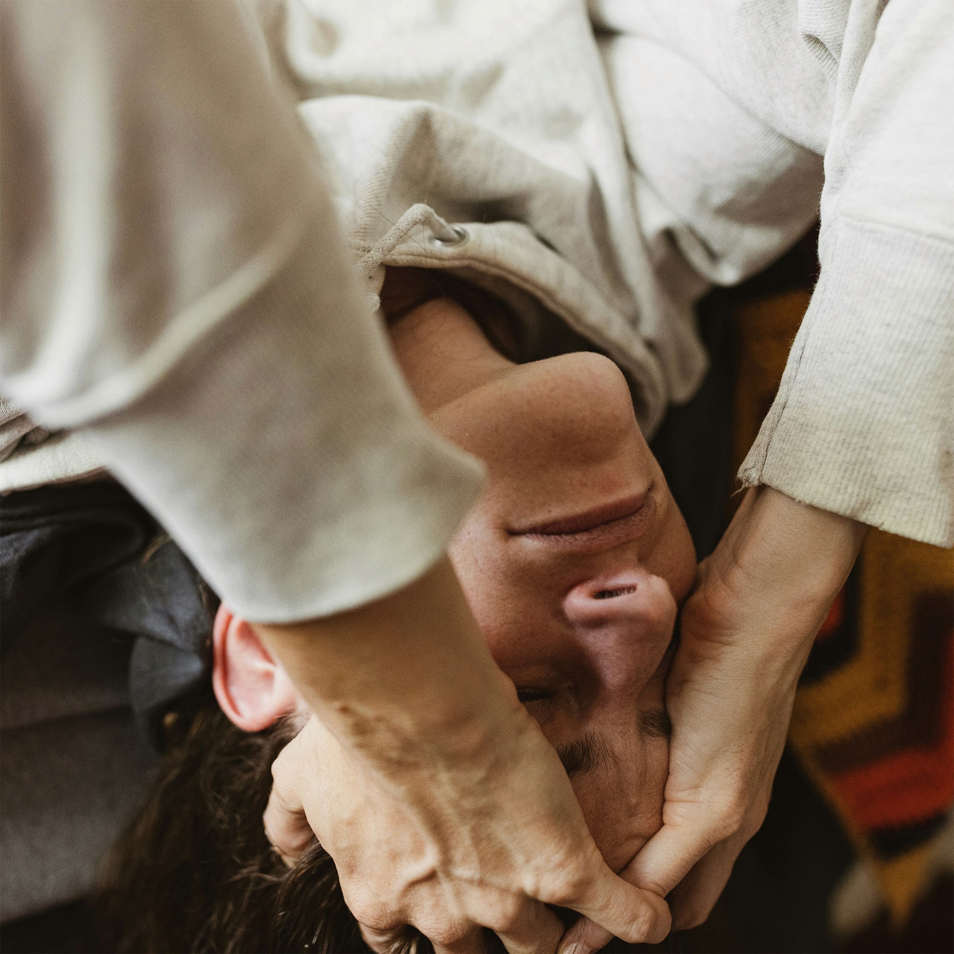 a photo of a woman with brown hair hanging off the end of her bed upside down with her hands covering her face in distress