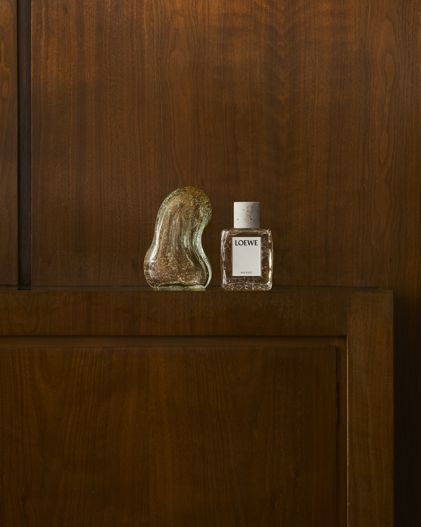 LOEWE Iris Root fragrance displayed on a walnut cabinet alongside a sculptural crystal object within Antonio Lamela’s studio.
