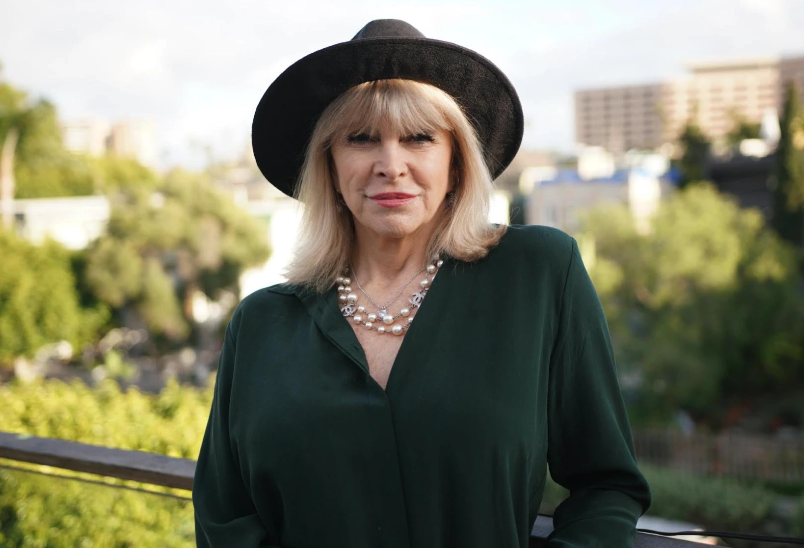 Marisa Peer in a dark green silk blouse and black hat, posing outdoors as a symbol of confidence and the Genie Within You lifestyle.