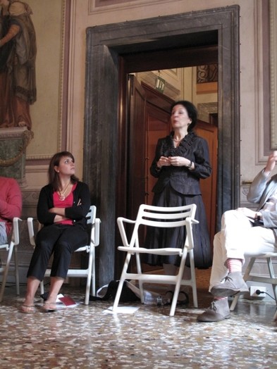A photo of a woman giving a lecture while sitting in a renaissance era room.