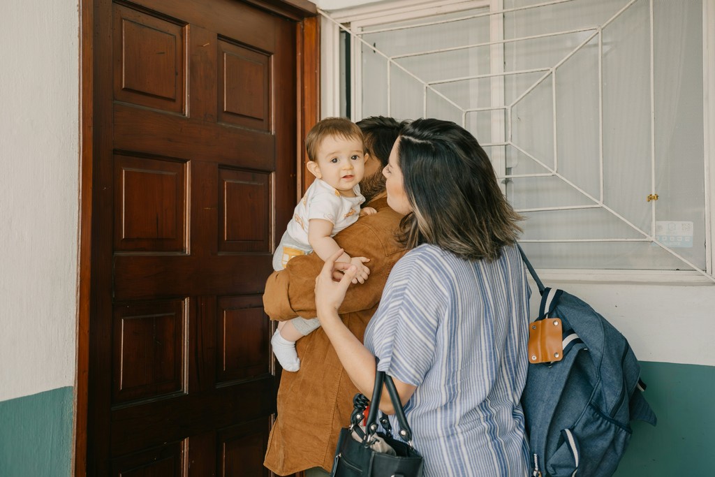 A family stands by the doorway, with the father holding a baby and the mother leaning in for a kiss, conveying warmth, love, and the comfort of home.