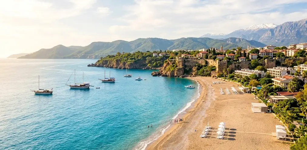Antalya'nın turkuaz denizi, tarihi kalesi ve lüks sahil mülklerini gösteren panoramik plaj manzarası.