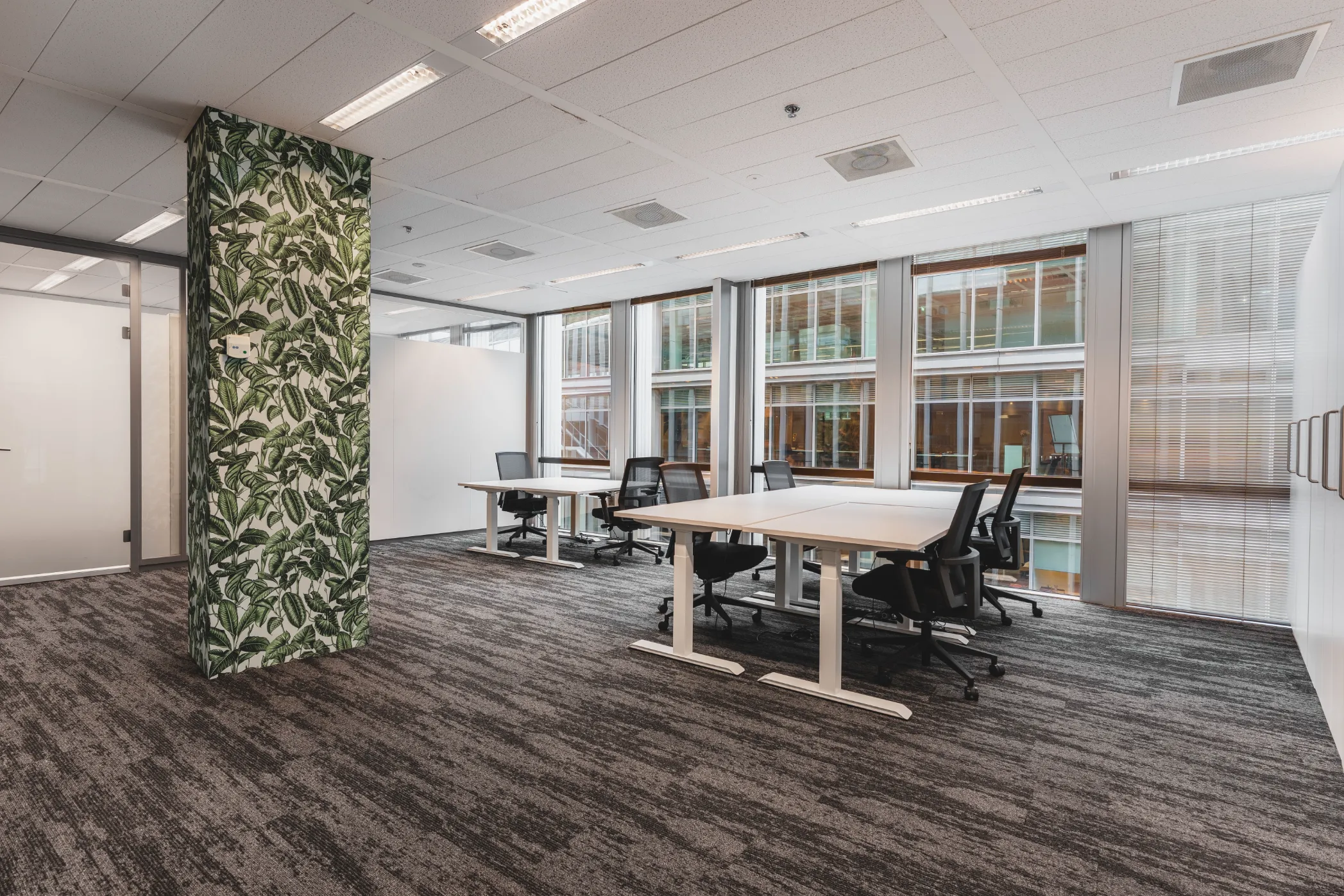 Kantoorruimte met bureaus, planten en uitzicht op de omgeving