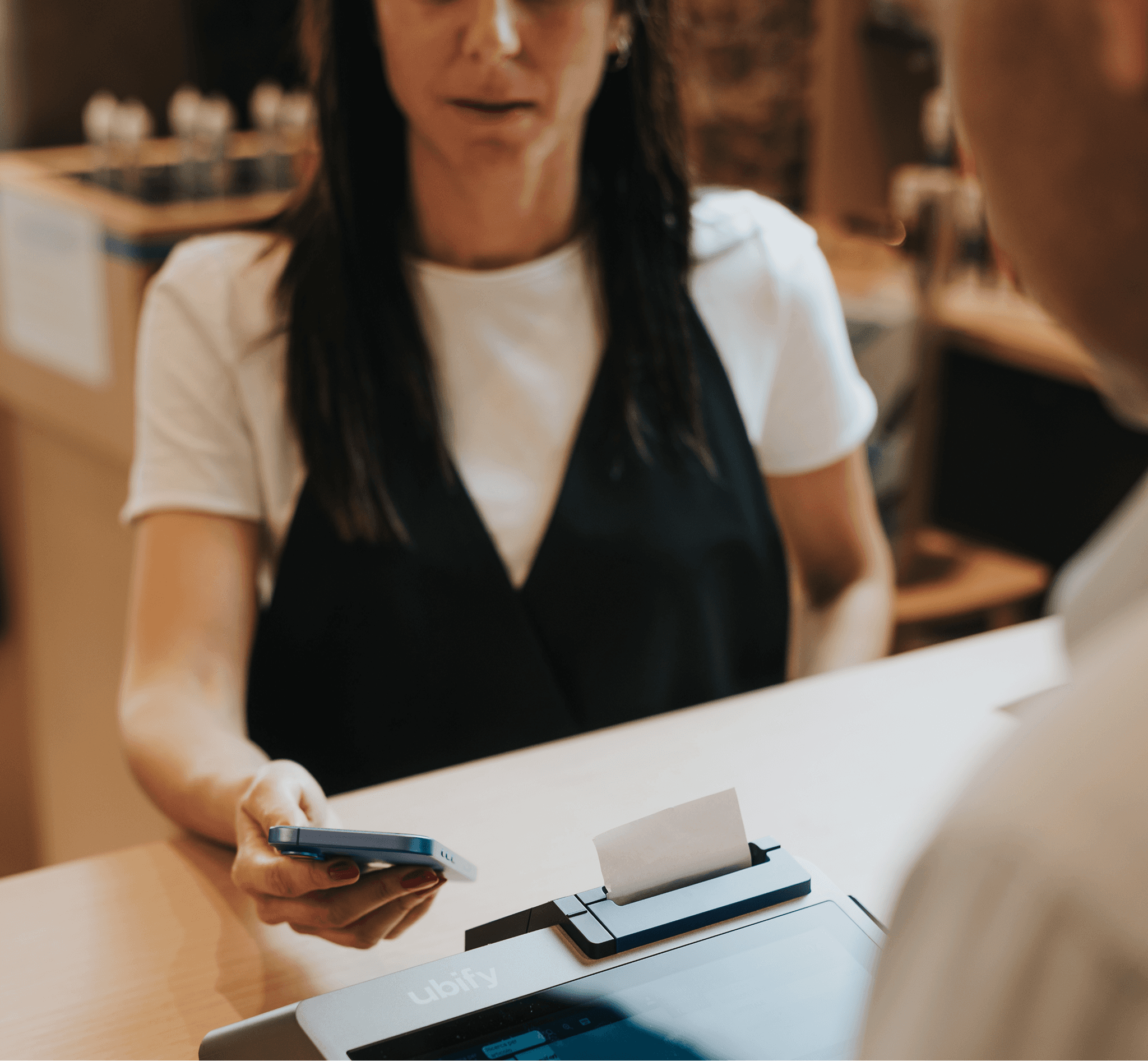 Cliente porge lo smartphone per pagare alla cassa Ubify, posizionata sul bancone di un punto vendita.