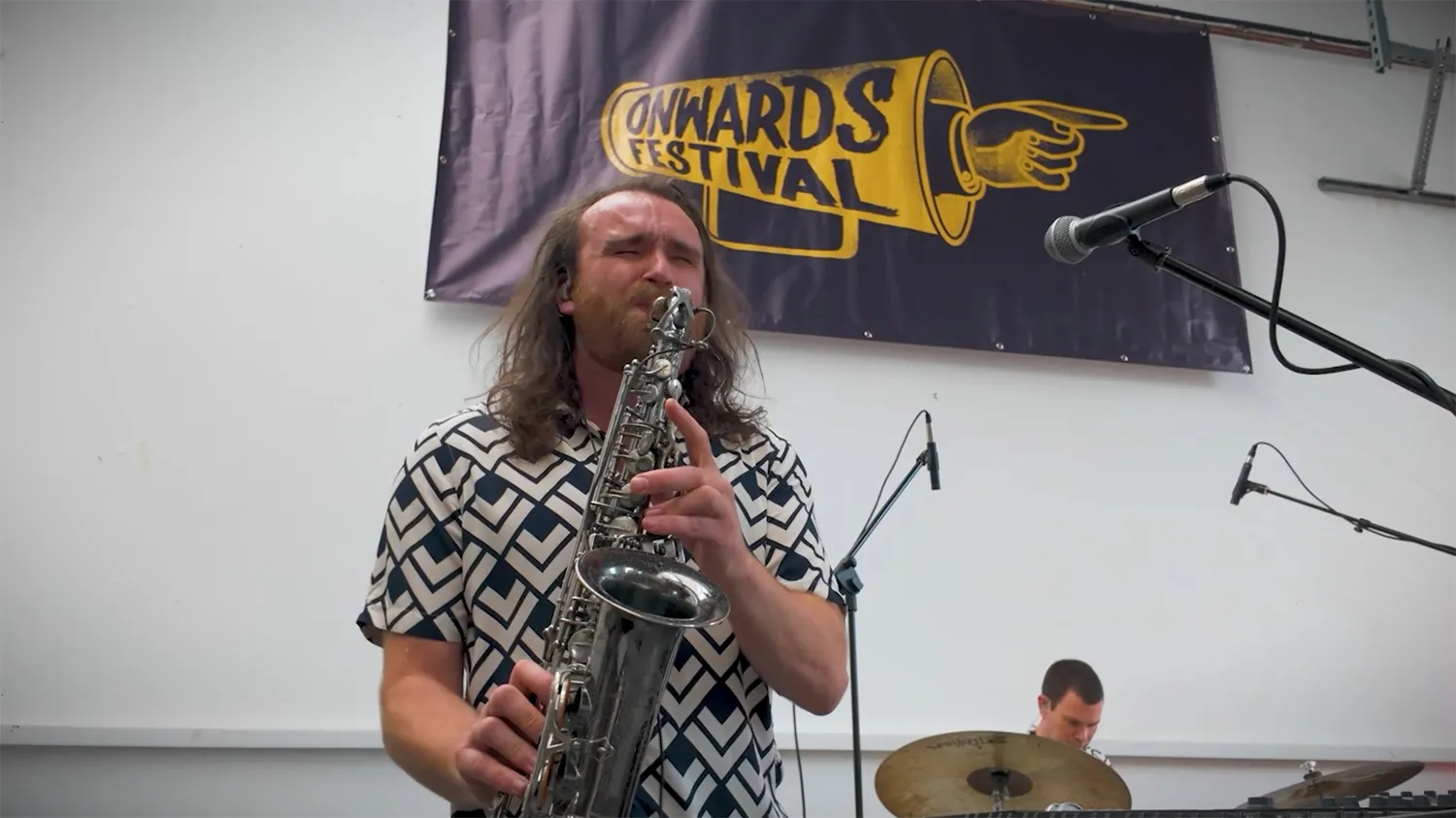 Saxophonist performing live on stage at the Onwards Festival, with band members behind him.