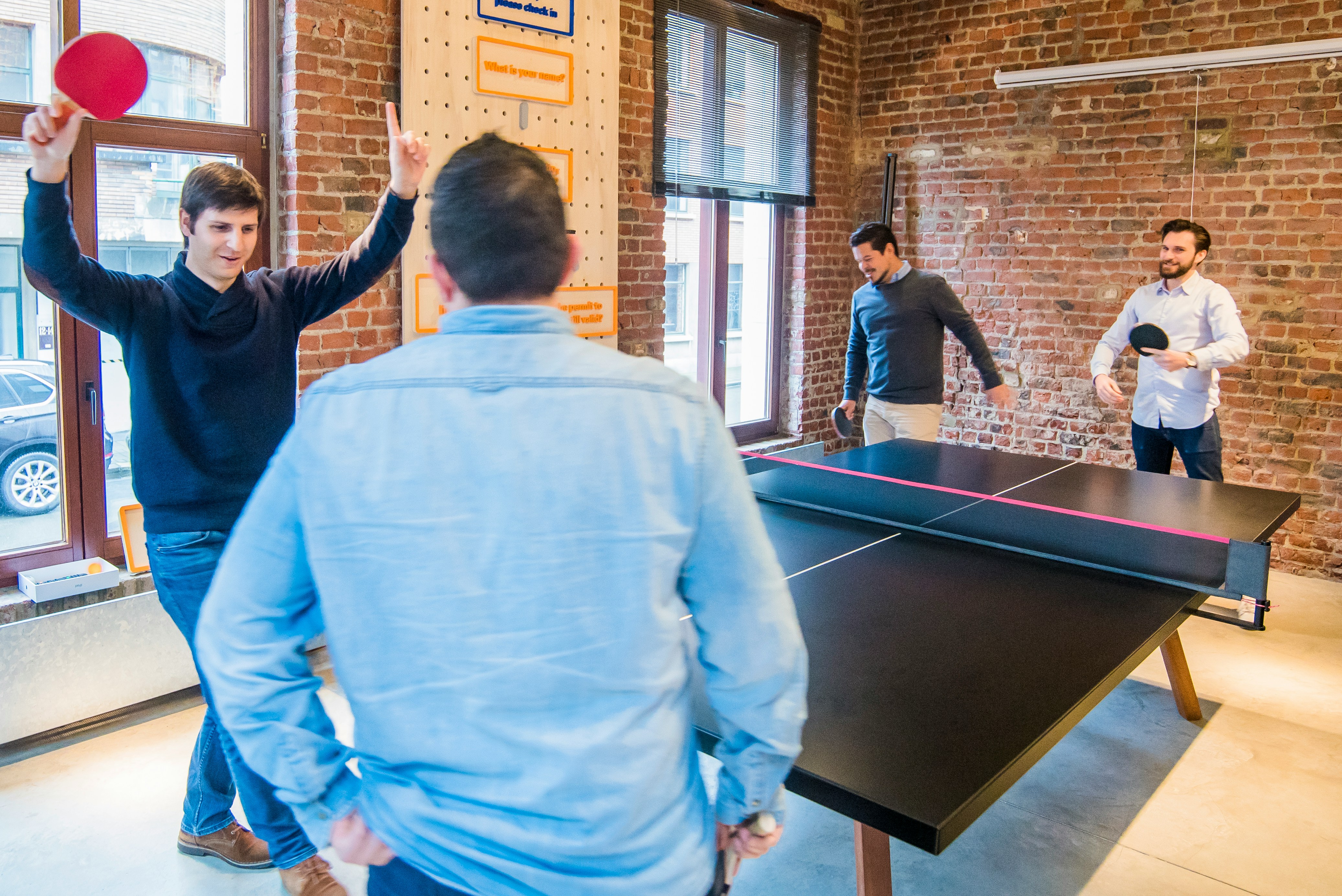 Four colleagues enjoying a friendly game of ping-pong in an office setting.