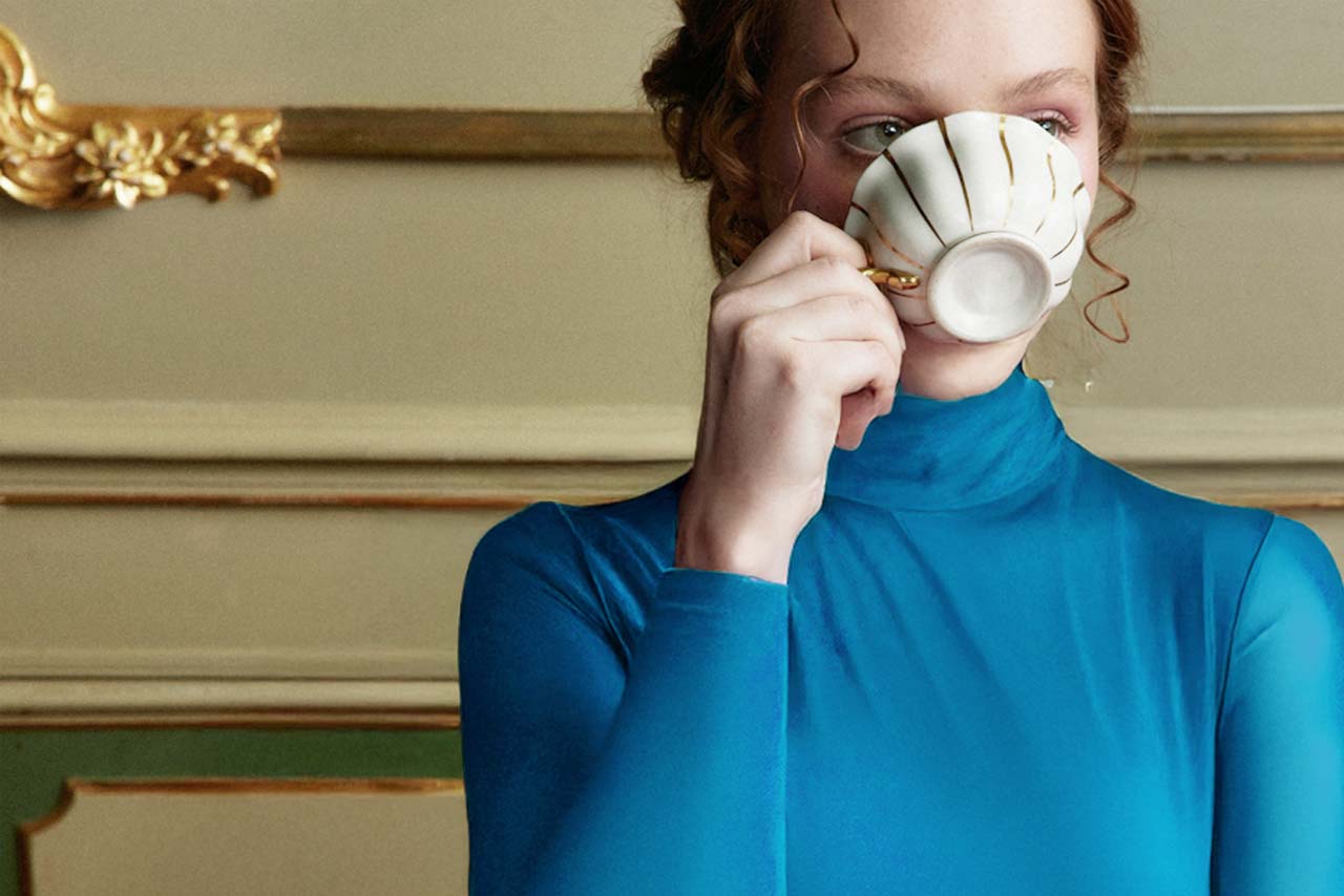 A black and white aerial photo of a tennis player in a white outfit preparing to serve, viewed from directly above.