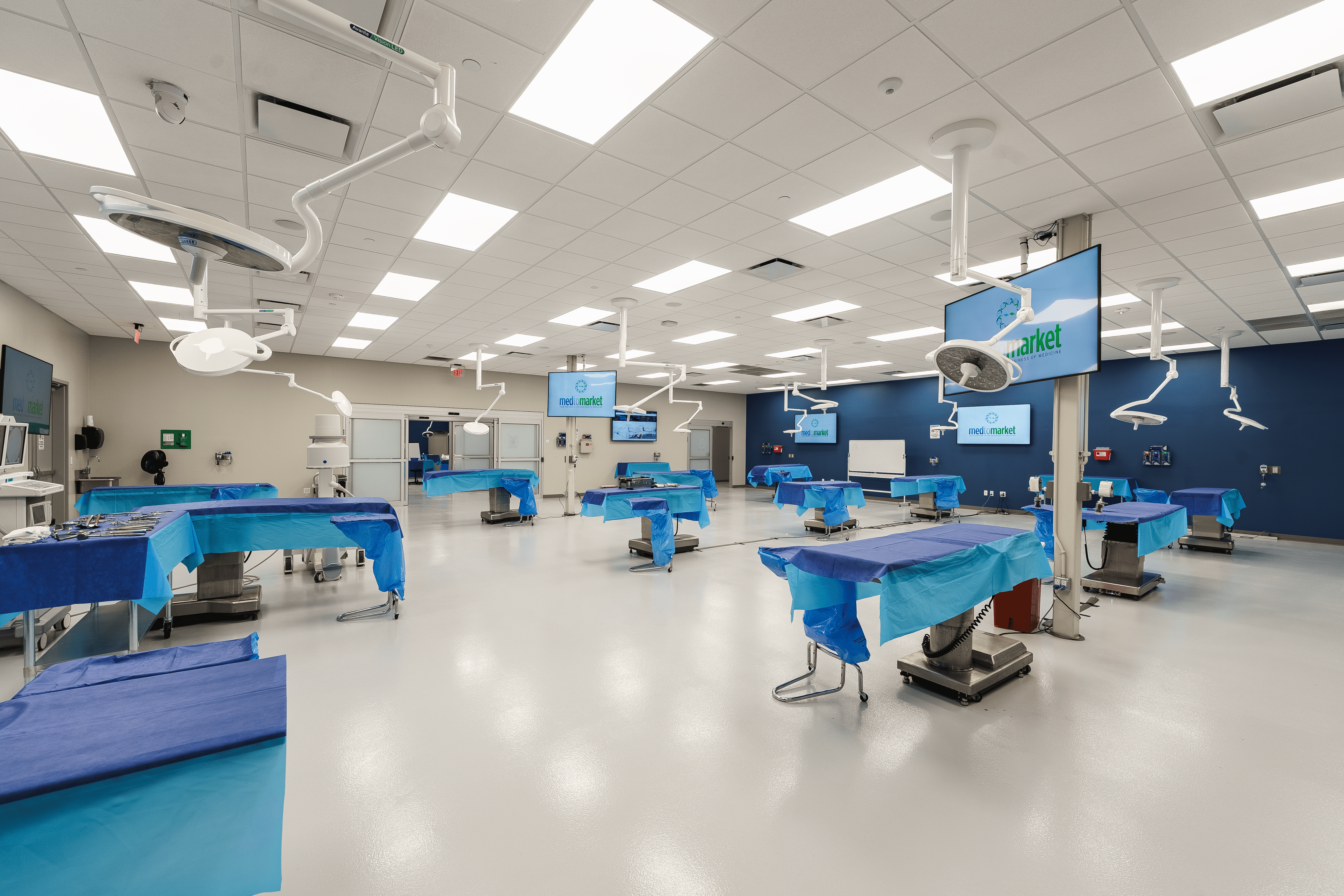 A young person with curly hair smiles at the camera while sitting in front of a laptop against a dark background.