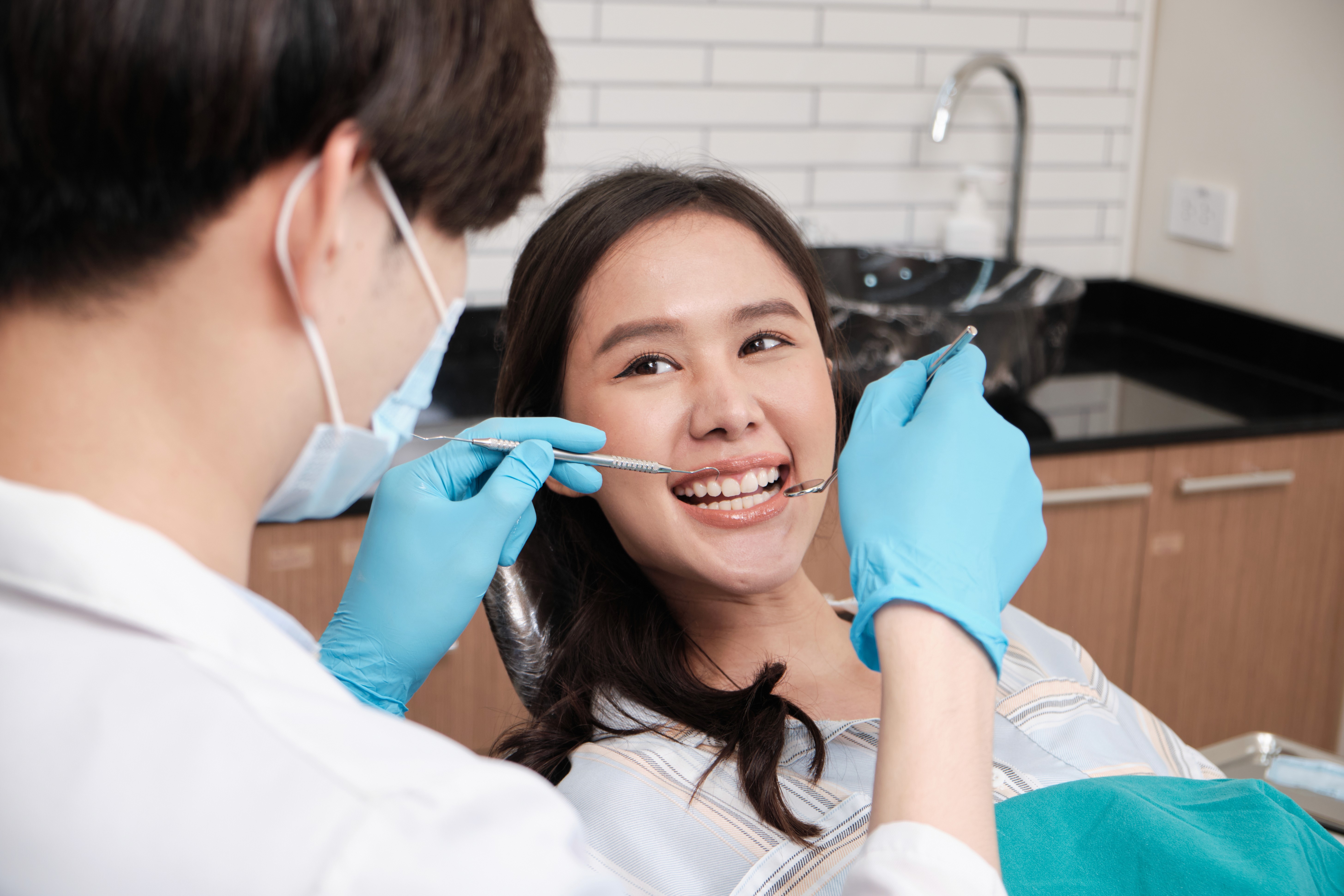 Asian male dentist checks young female patient's teeth at dental clinic.