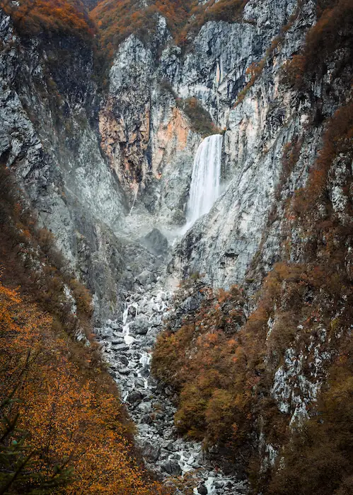 The massive Boka Waterfall in the Soča Valley, cascading down a rugged mountain face surrounded by colorful autumn trees.