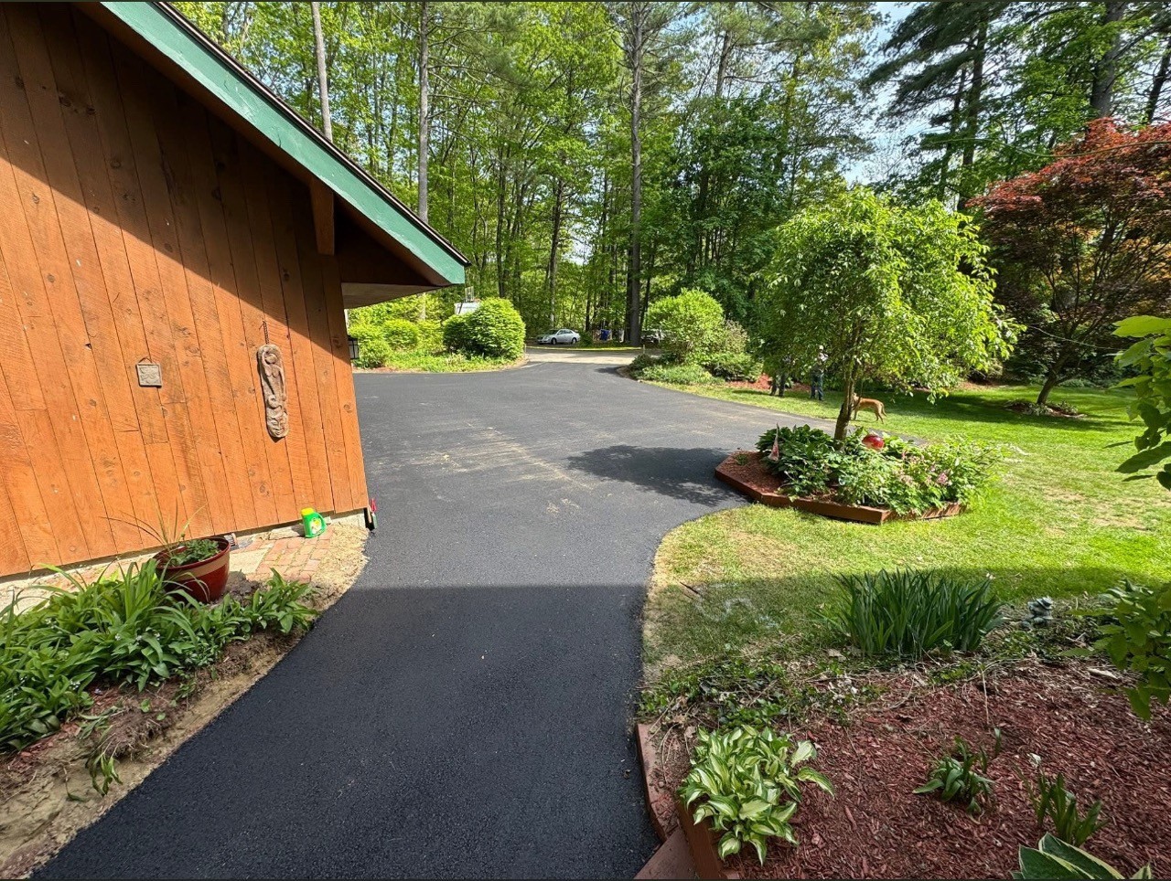 Finished asphalt driveway curving past a cedar home and gardens