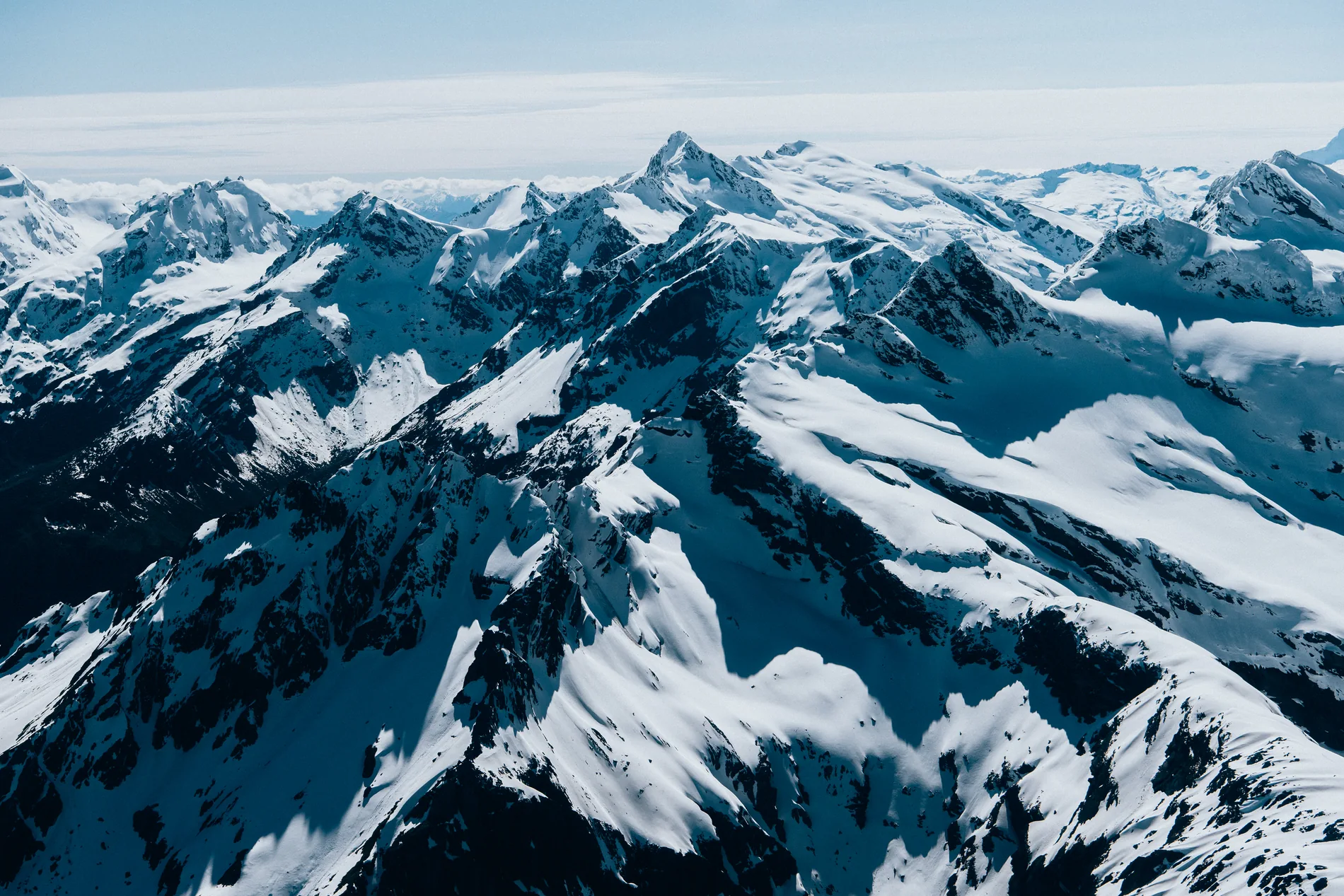 Aerial across a range of sharp snow-covered peaks under a clear sky
