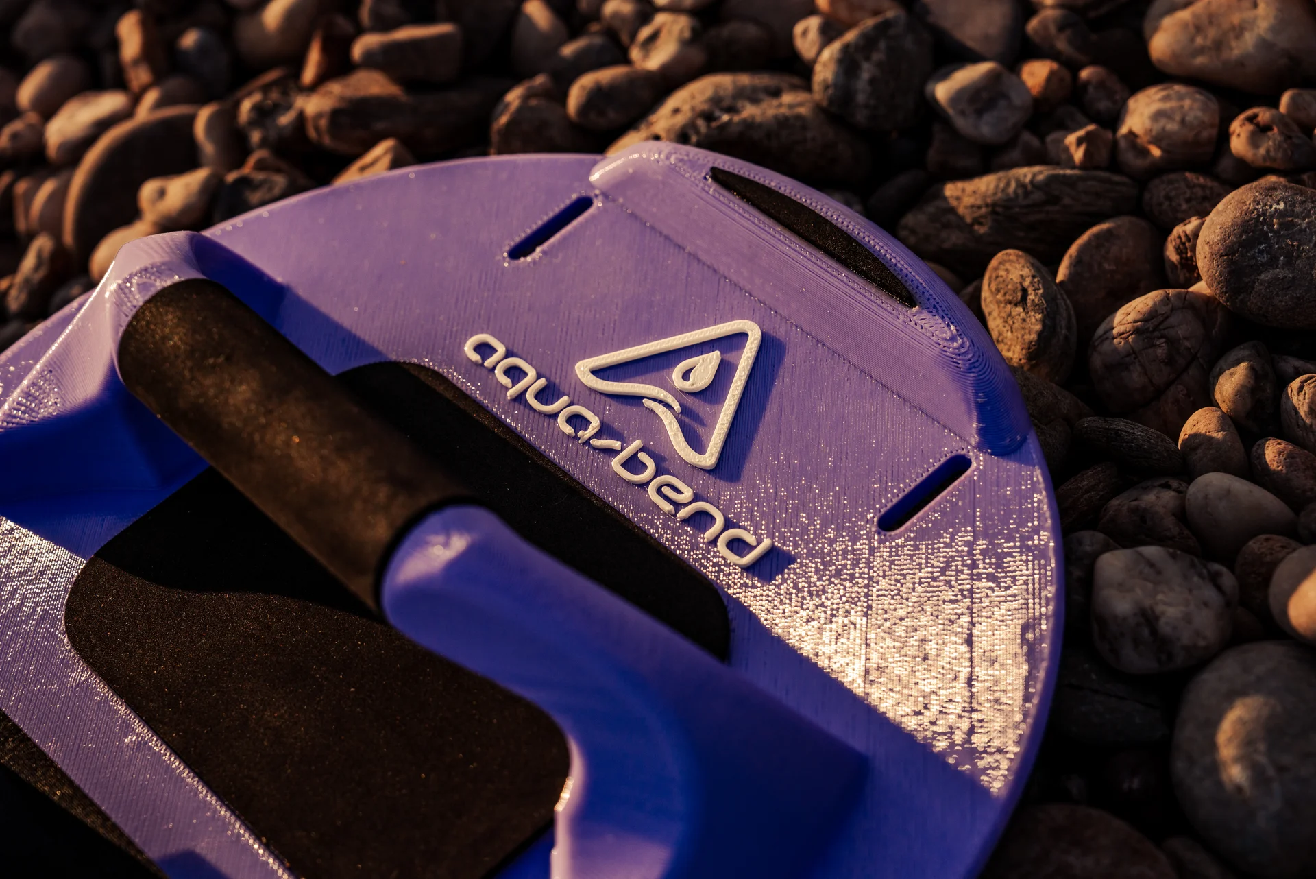 Close-up of Aqua-Bend FLOW disc in violet on beach rocks, showing grip texture and large white Aqua-Bend logo