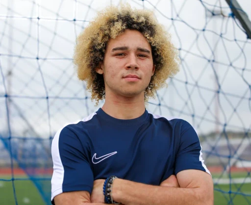 Confident youth soccer player standing in front of a goal net on the field, ready for the game