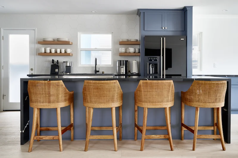 Kitchen island with bar stools, open shelving, and stainless-steel appliances in Costa Mesa Exterior Remodel. Photo by Todd Huge.