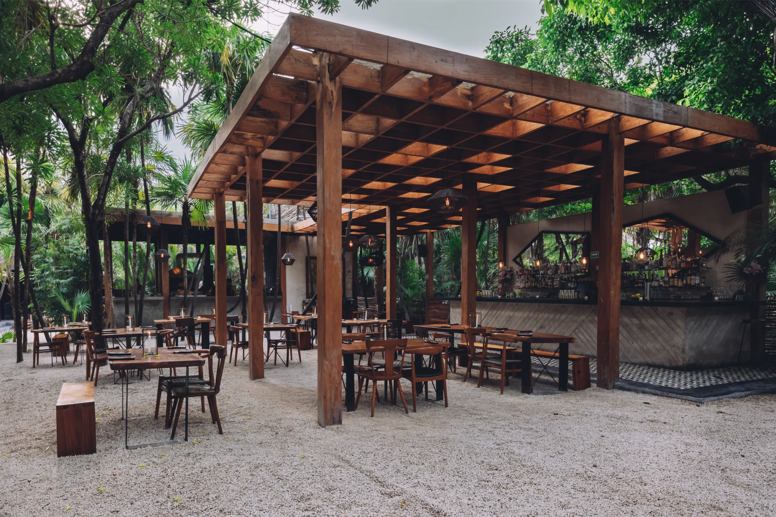 Wide view of Arca's open-air architecture featuring heavy timber columns and a wooden grid canopy integrated into the Tulum jungle.