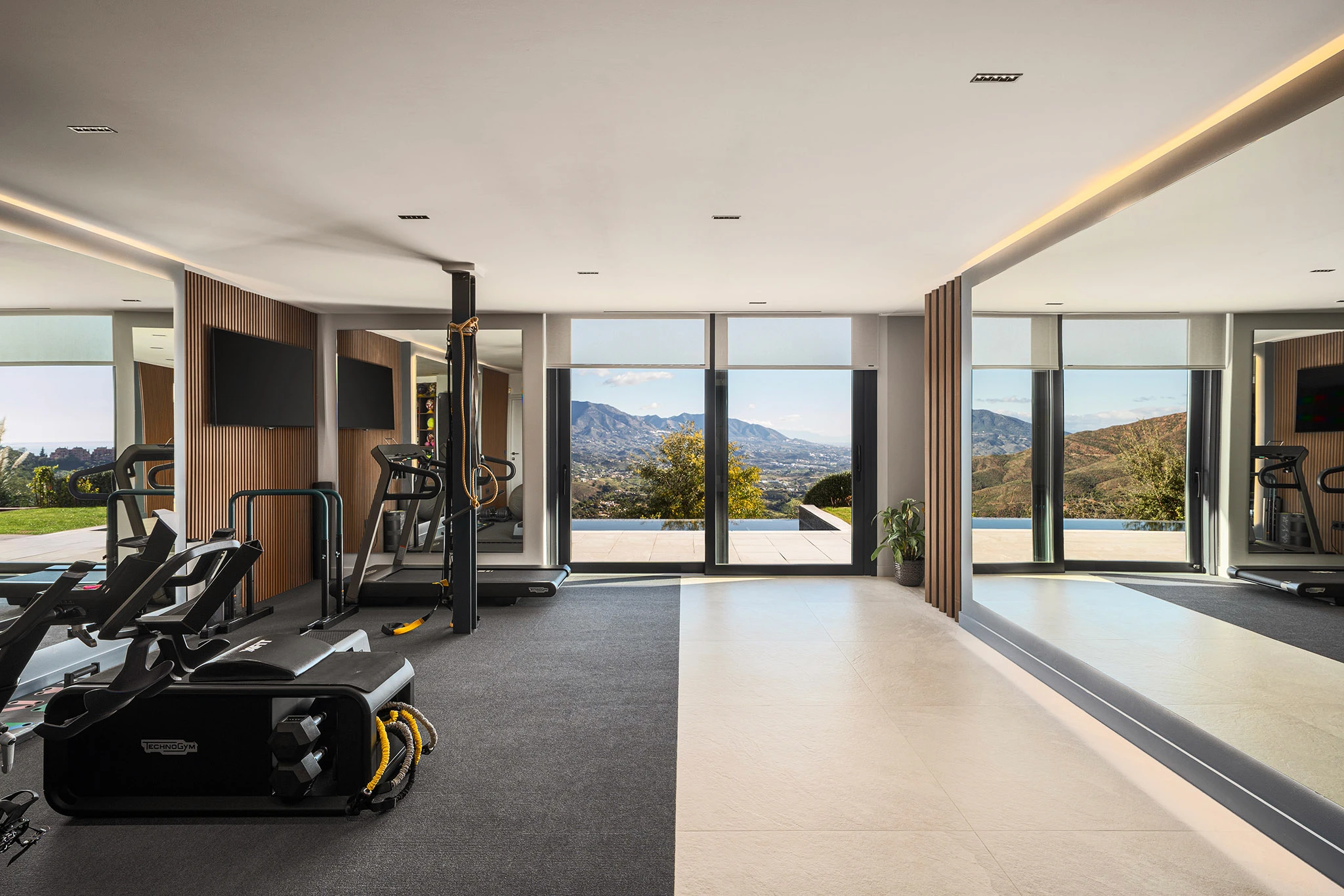 Villa Vista Marbella home gym with cardio equipment, mirrored wall, and mountain-view glazing