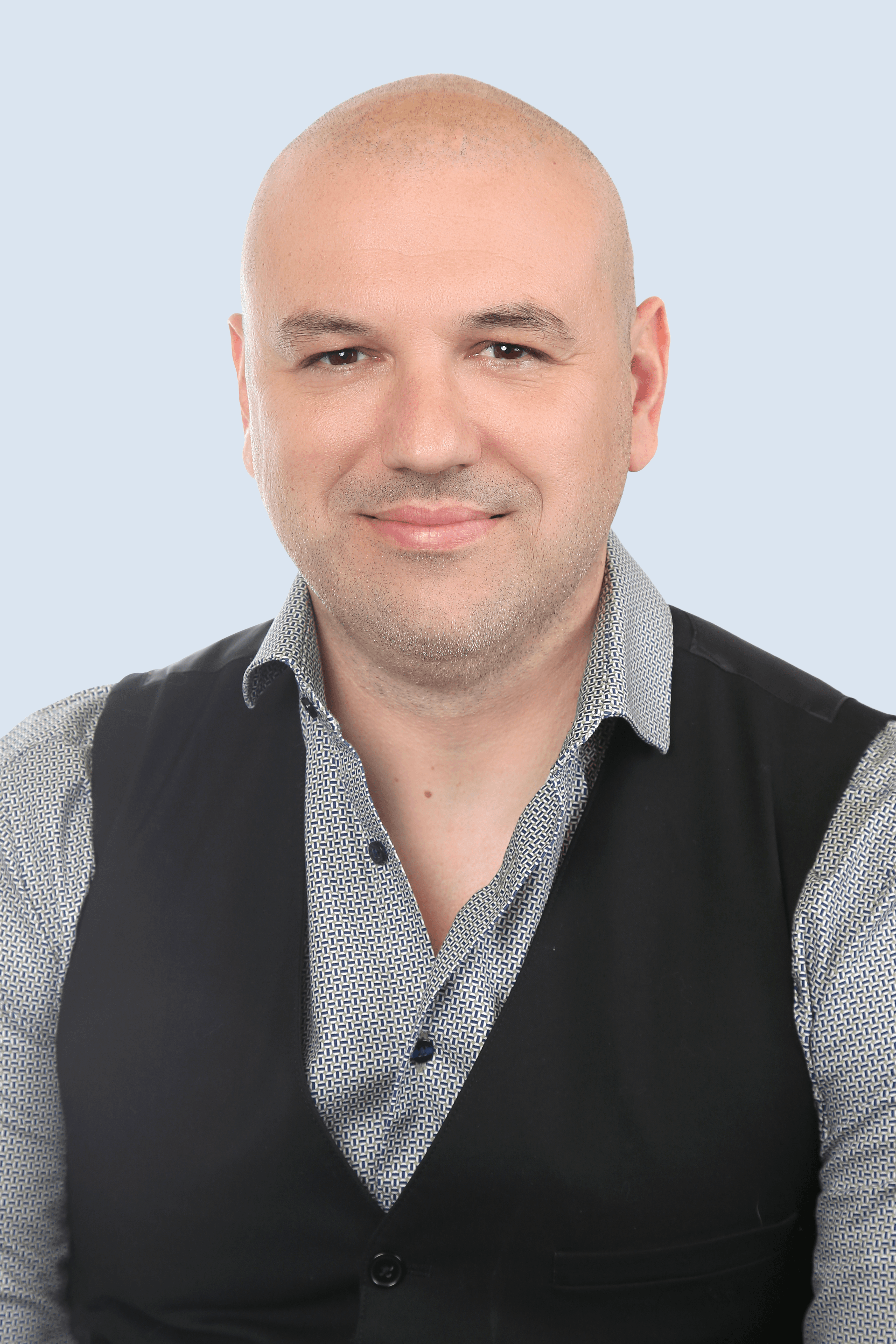 Frau mit braunem Anzug, blauem Hemd und Brille schaut mit verschränkten Armen seitlich in die Kamera und lächelt. 