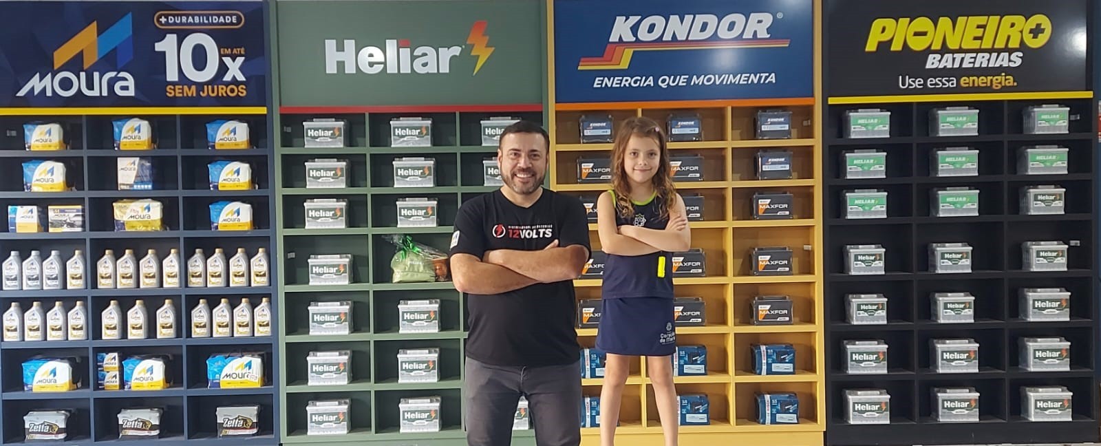 Miguel e criança diante do painel multimarcas de baterias