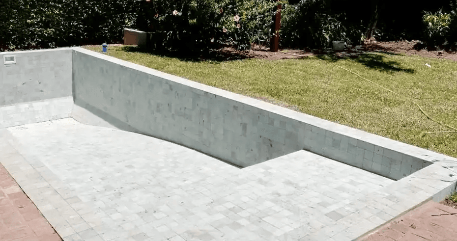 Construcción de pileta de hormigón en jardín, mostrando la colocación de revestimiento premium de Piedra Bali en tonos claros.