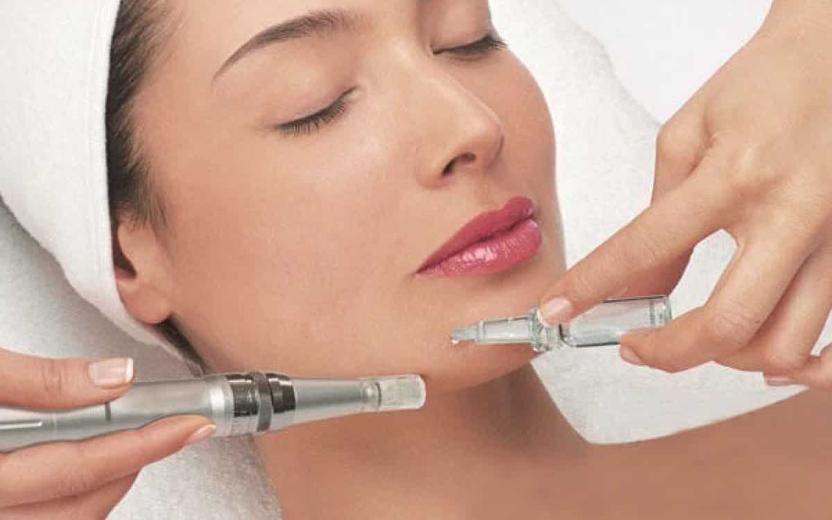 A woman lying down with a towel wrapped around her head, her face glowing with facial oil. She has a peaceful expression, enjoying a skincare treatment.