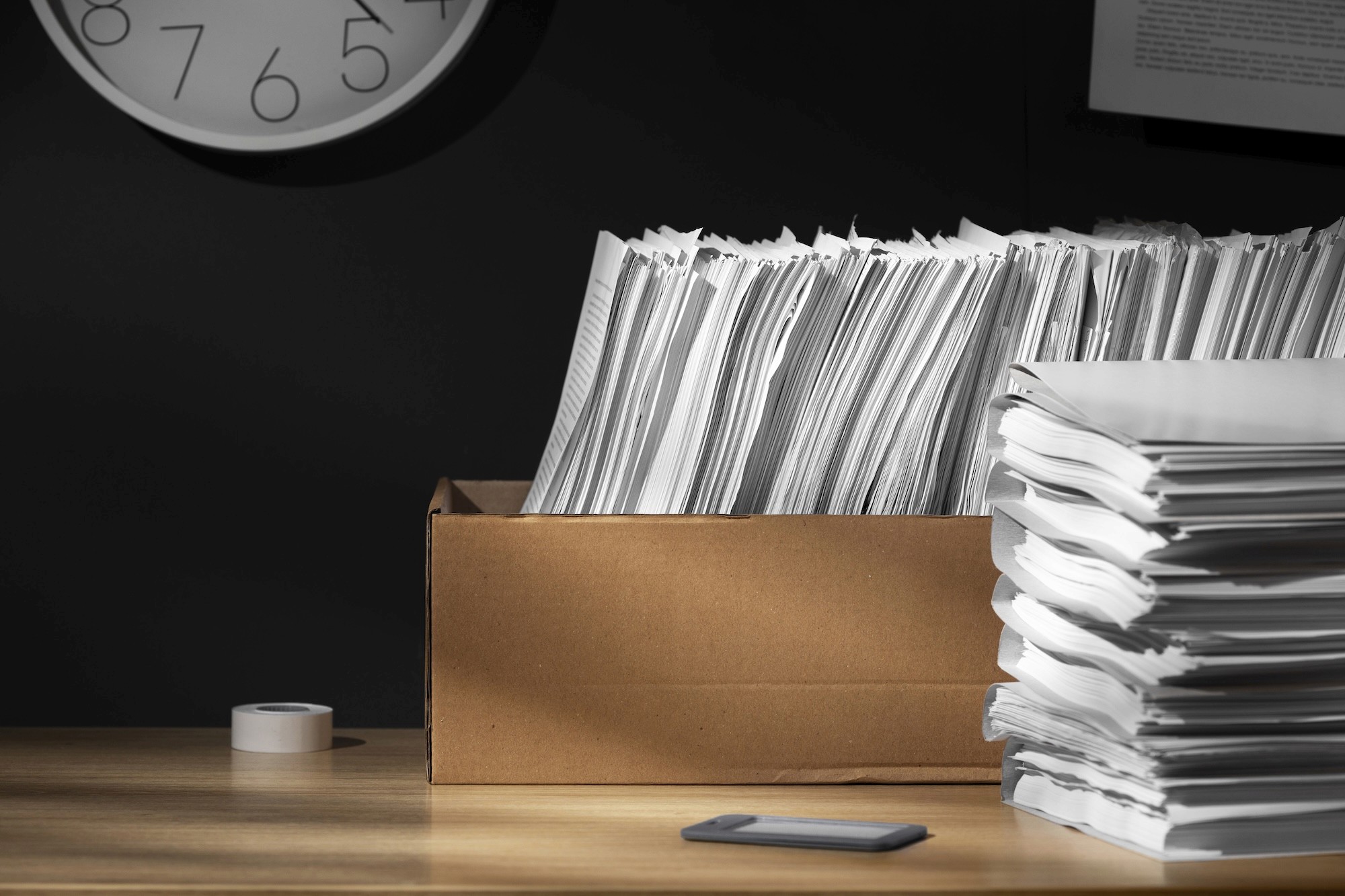 stacked and unstacked documents, on a brown desk and a wall clock on a black background