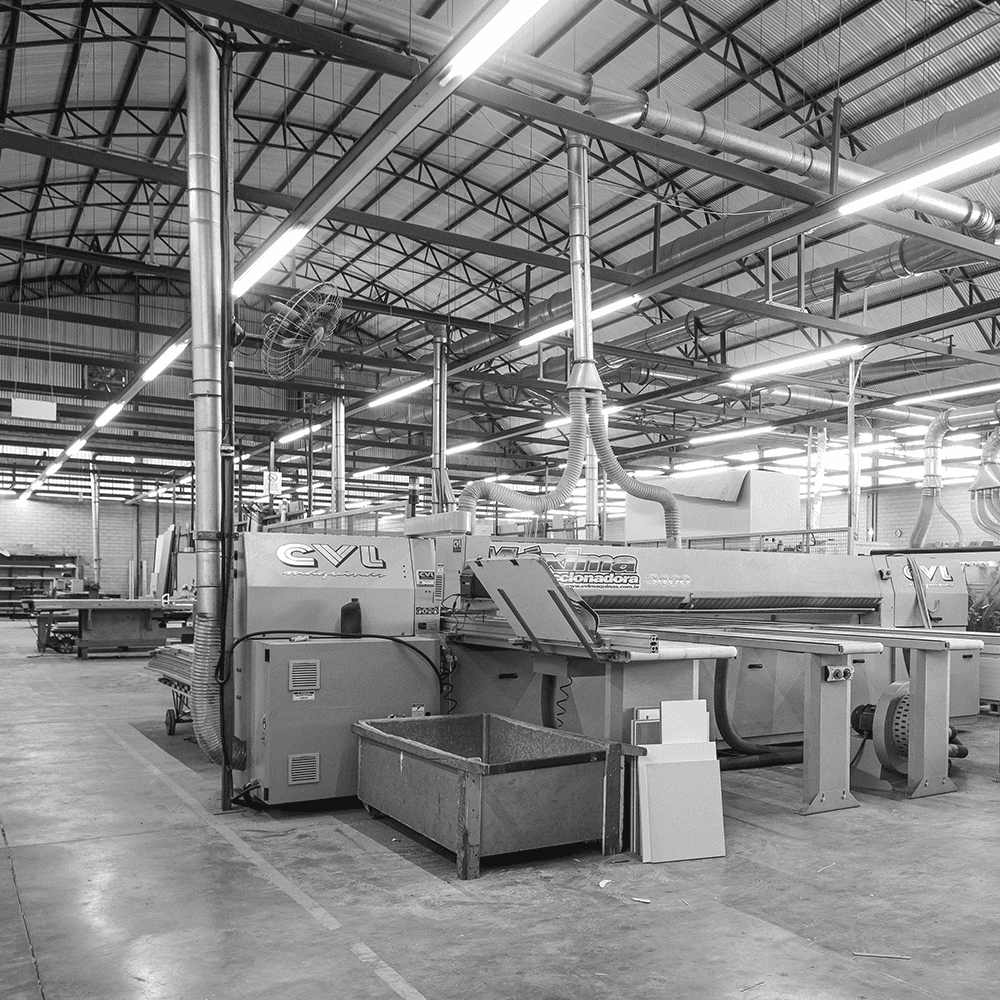 Industrial woodworking facility featuring a large CVL Máquinas panel saw and dust extraction system in a black and white factory setting.
