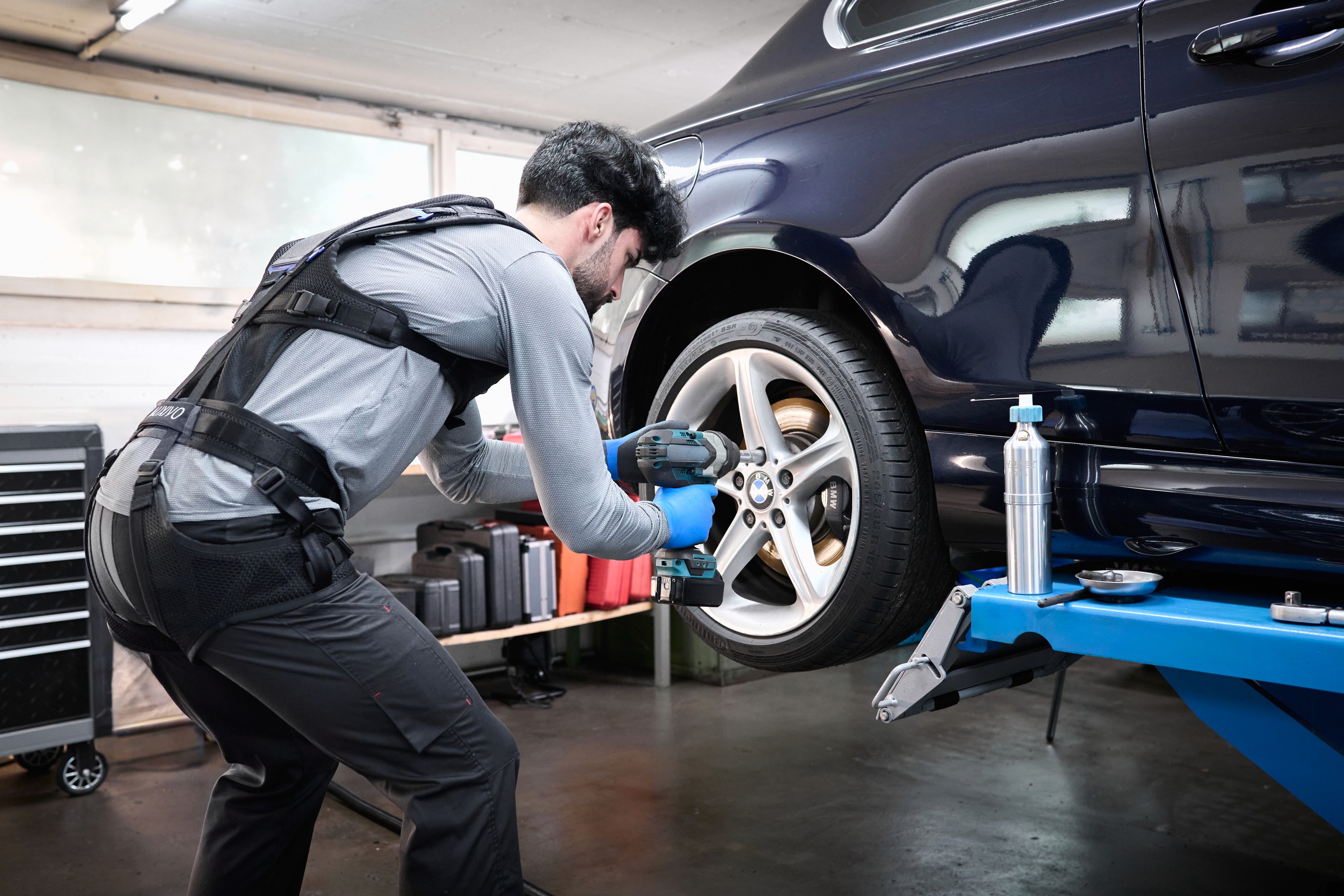Homme mécanicien portant un exosquelette et changeant une roue sur une automobile.