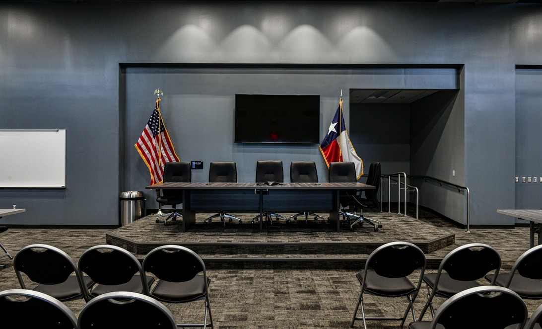 Boardroom with elevated dais and US and Texas flags at Bridgestone MUD Operations Center, by Martinez Architects
