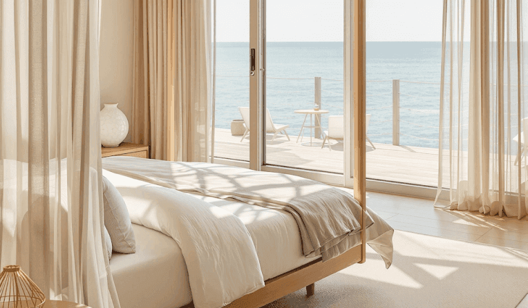 Serene bedroom with ocean view, sheer curtains, and cozy neutral bedding.