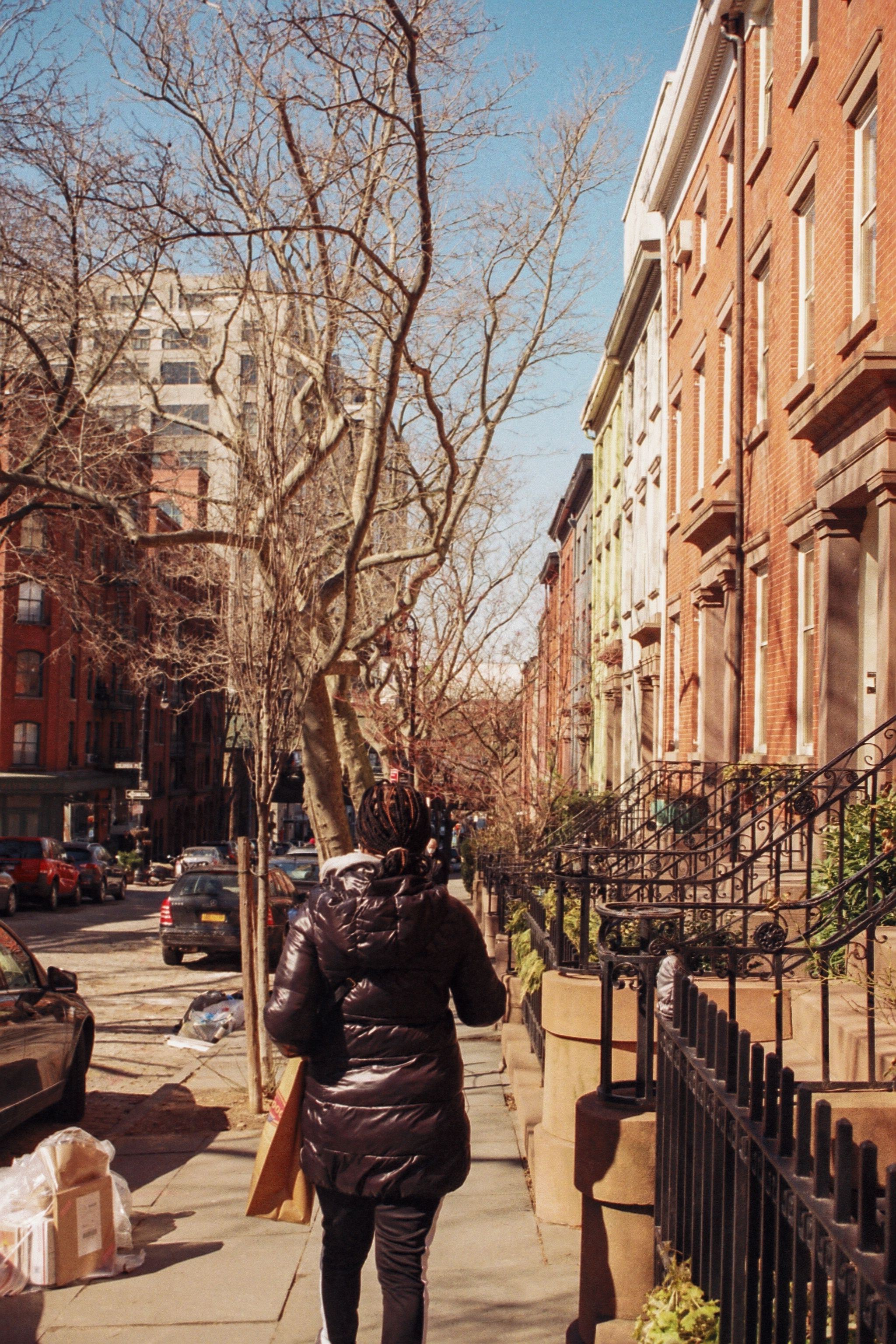 A woman walks alone along a brownstone-lined city street.