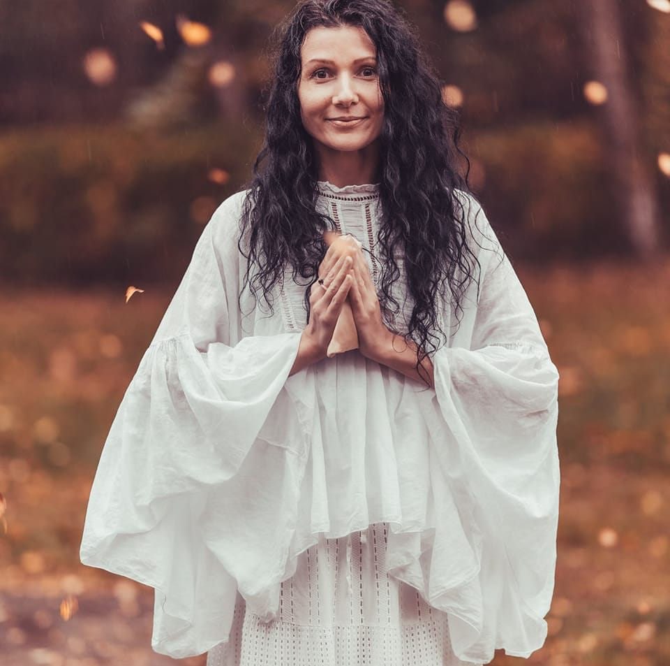 Smiling female therapist with short gray hair, wearing a brown top and a purple shawl, surrounded by a cozy background.