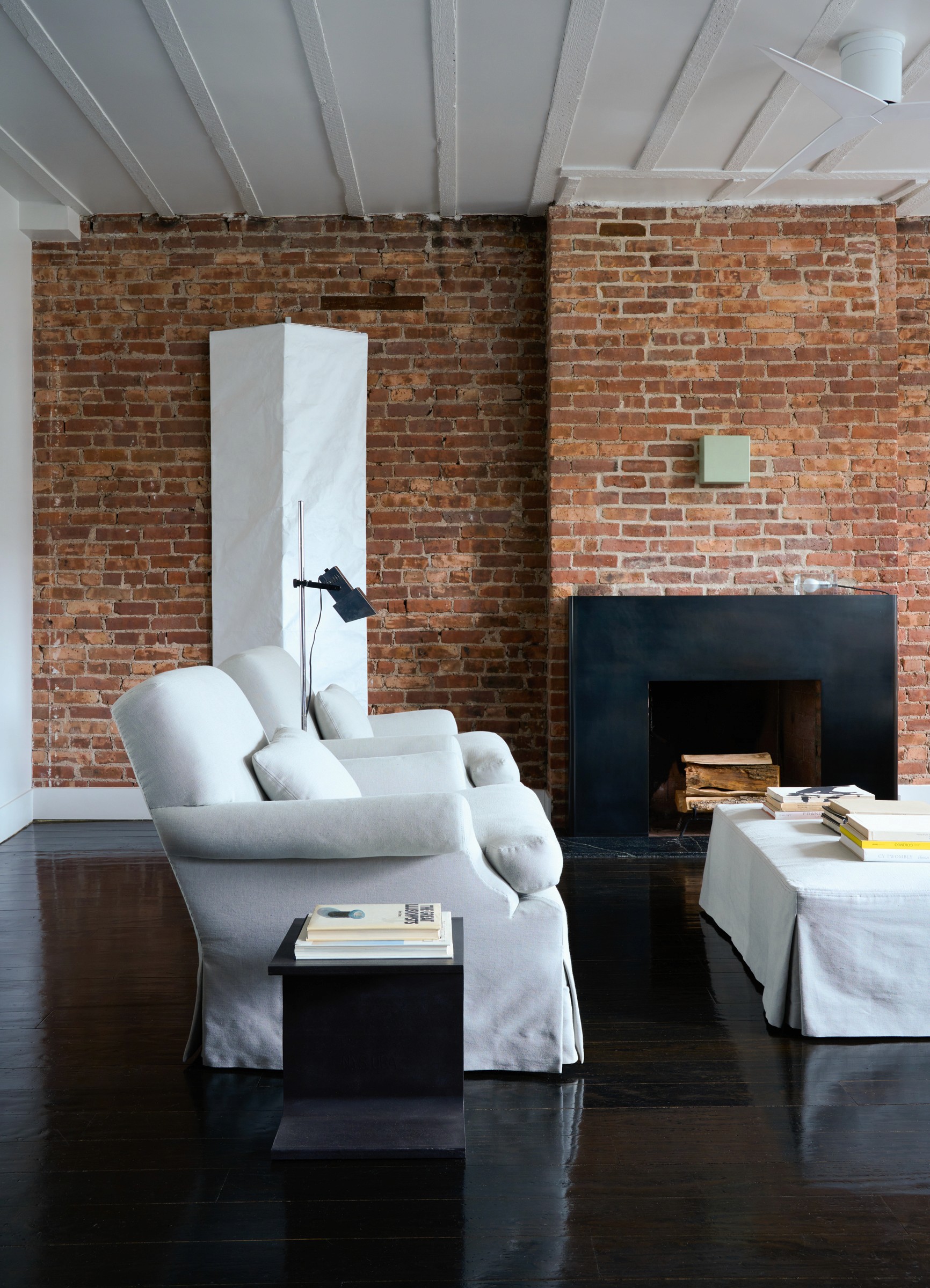 Living room with dark metal fireplace, oversized paper sconce, and matching custom upholstered armchairs.