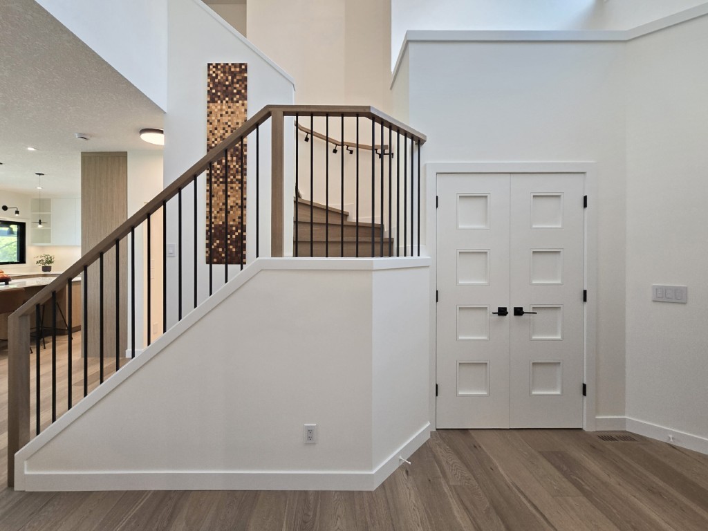 Image of Modern staircase with wooden railing and black metal balusters leading to upper level by KHD Homes.