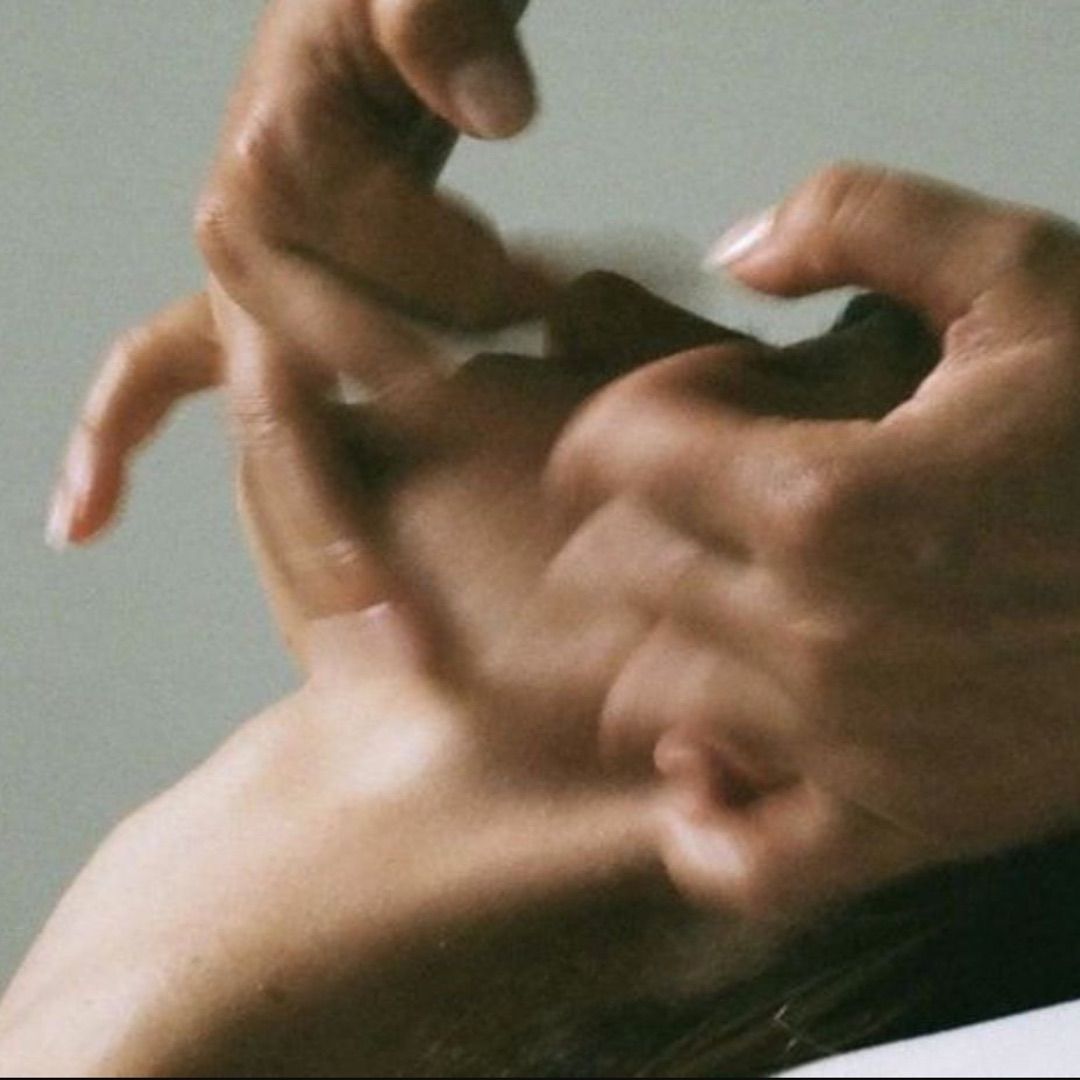 Woman sitting in sunlight with eyes closed, wearing relaxed neutral clothing in a peaceful setting.