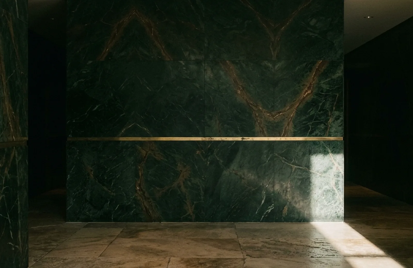 Dark green marble wall with a brass inlay line and a band of sunlight