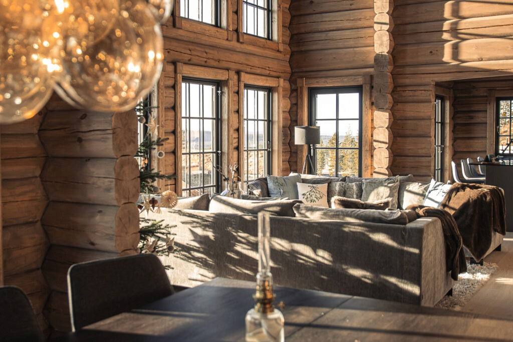 Spacious log cabin living room in Idre Himmelfjäll featuring large windows, wooden interiors, and plush seating.