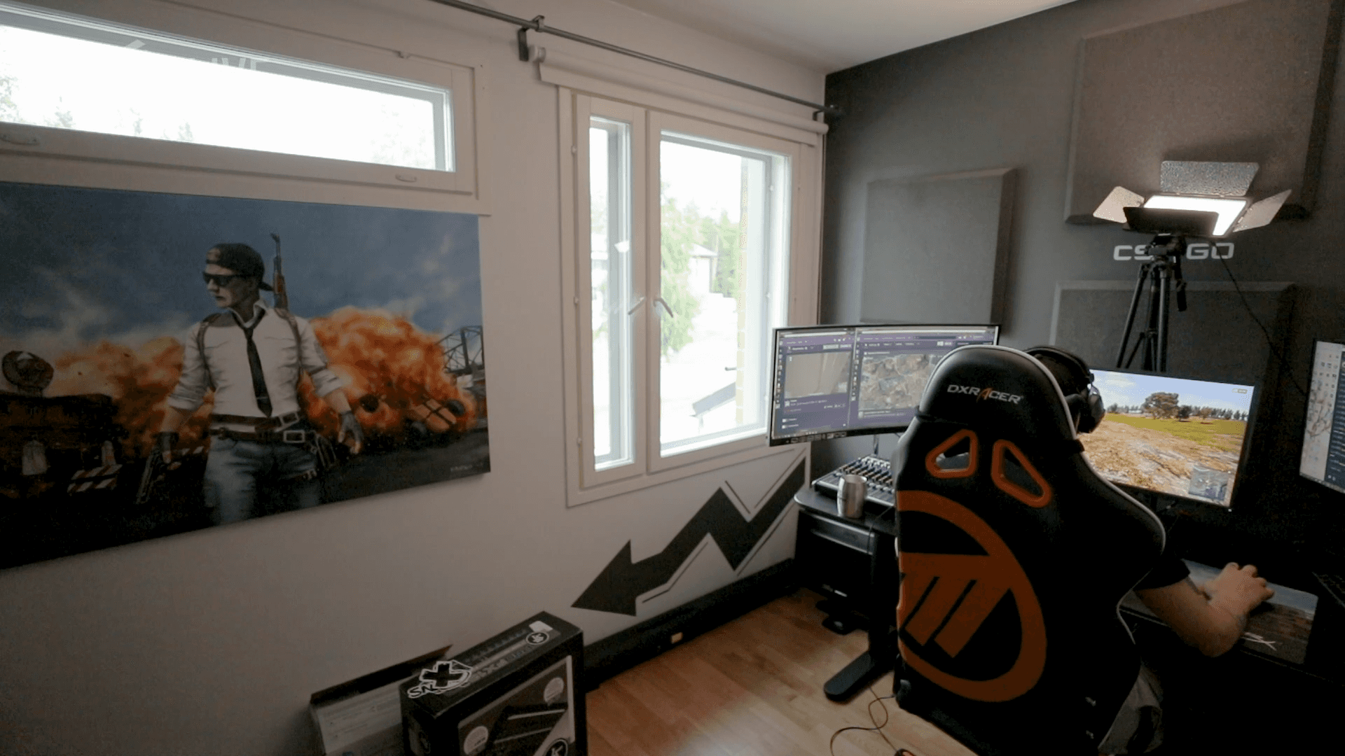 Wide shot streamer playing PUBG with back of chair to camera and large PUBG painting on wall. 