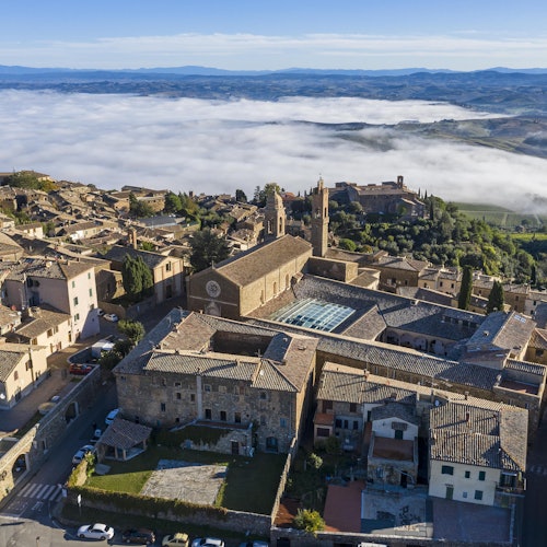 Aerial view of Montalcino, Italy, featuring historic buildings, a central courtyard, and surrounding countryside with low-lying fog.