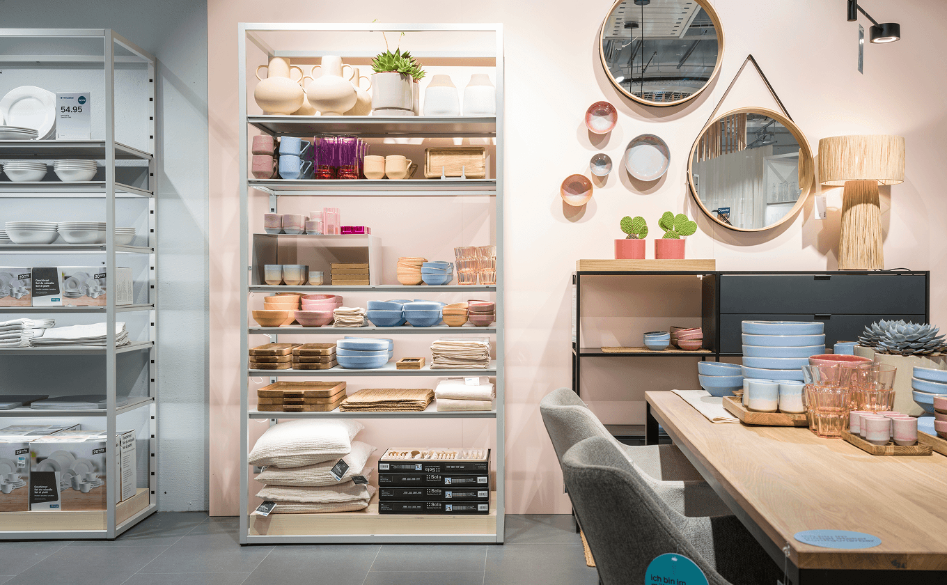 Innenaufnahme des micasa Experience Stores mit verschiedenen bestückten Regalkonfigurationen und farbiger Rückwand zur thematischen Zonierung des Raums.