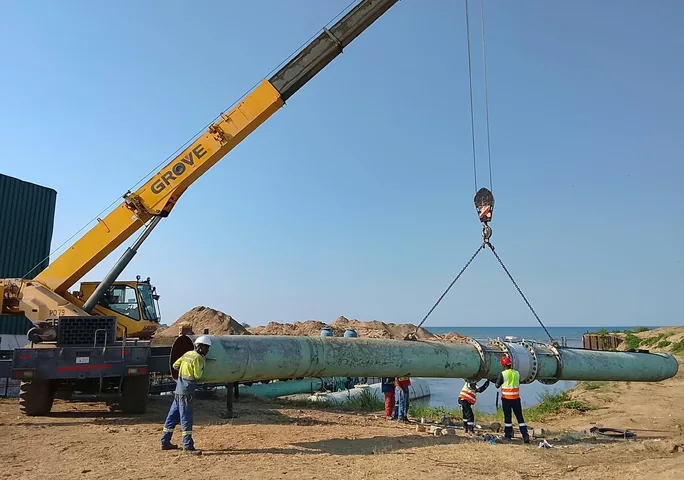 Site crew installing a large-diameter steel water main with a mobile crane