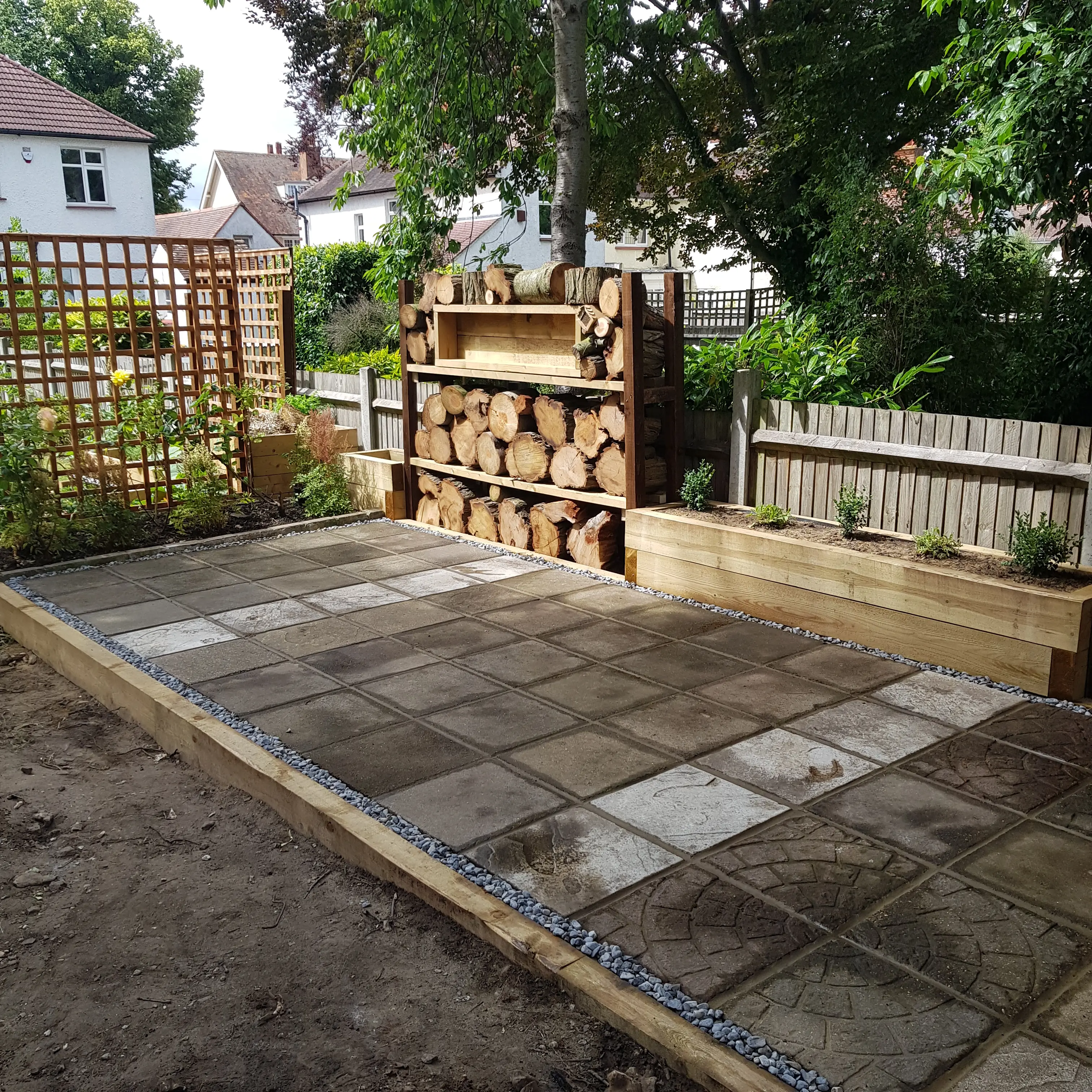 A landscaped outdoor space featuring stone paving, a wooden bench, and greenery in the background.