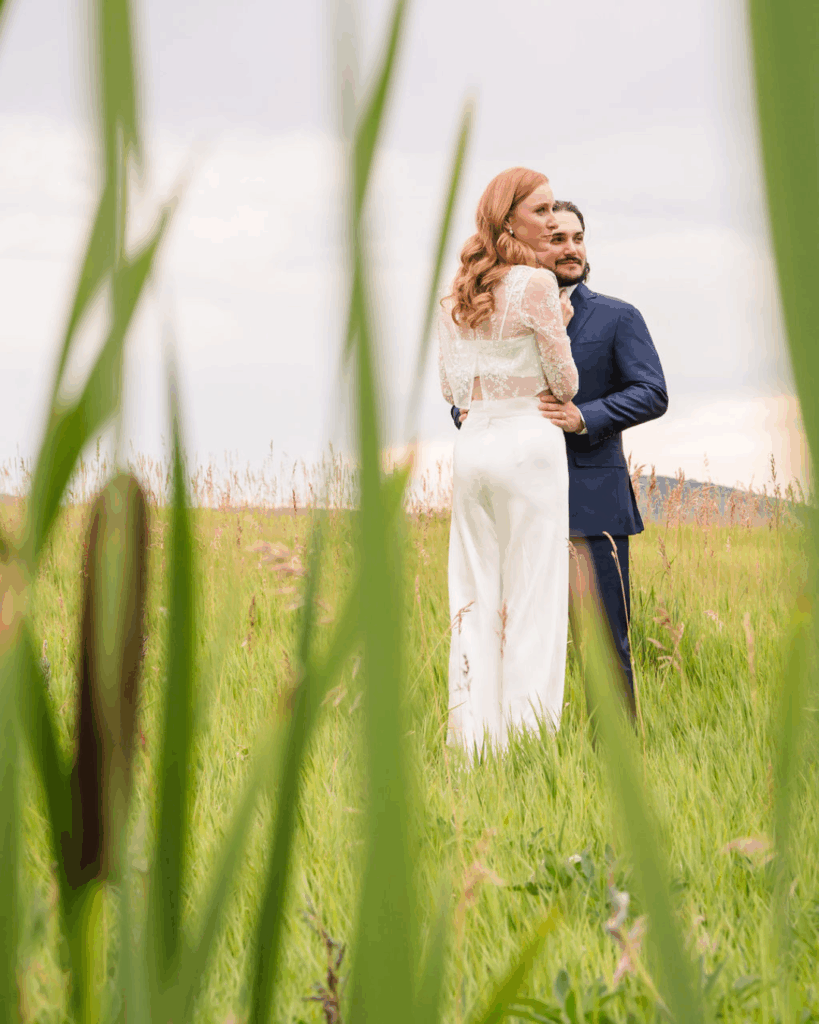 Newlyweds embracing in a meadow, viewed through tall grass