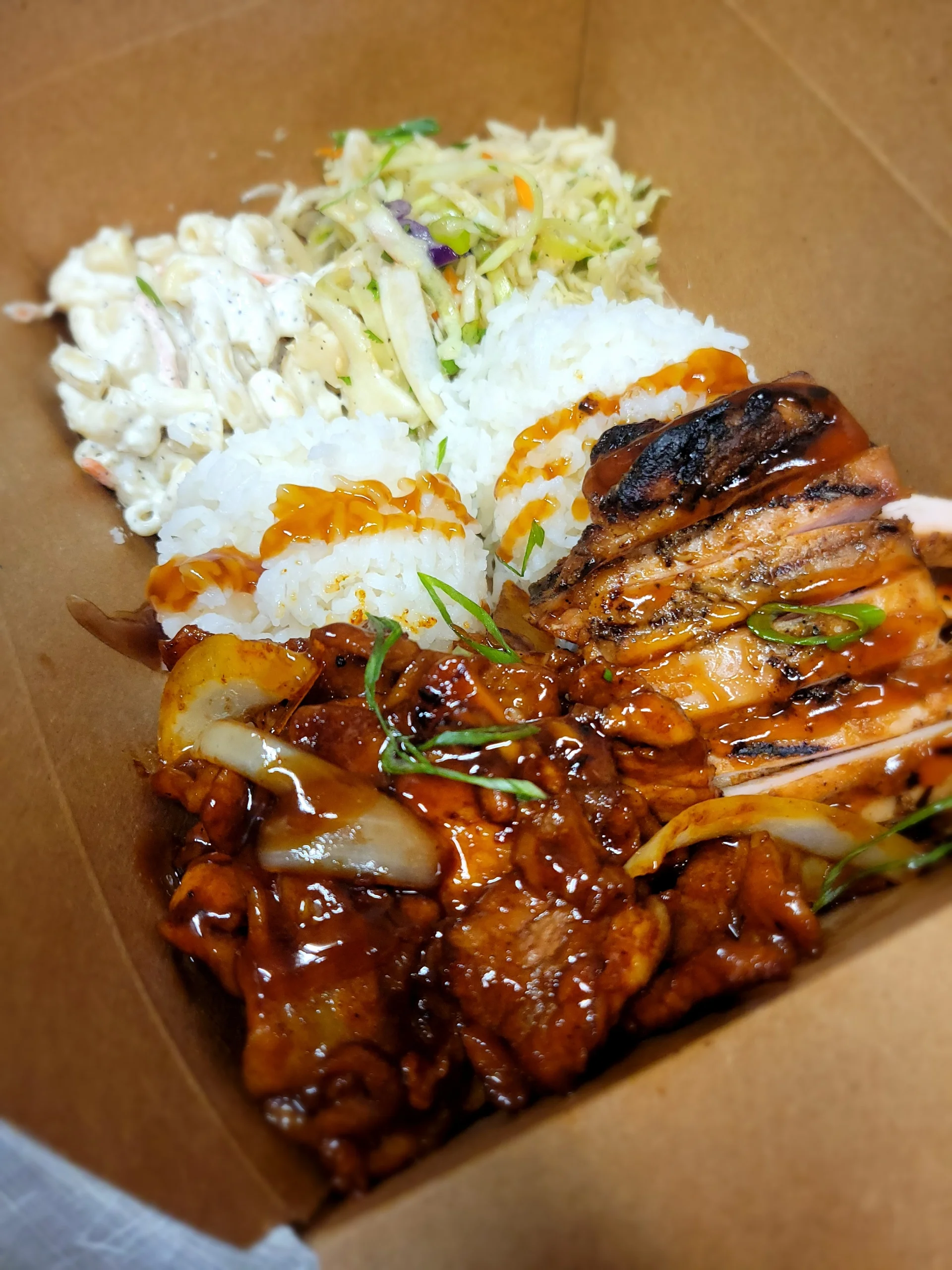 A Hawaiian BBQ combo plate featuring sliced char-grilled Huli Huli chicken and seared spicy pork with onions, served with two scoops of rice, mac salad, and slaw.