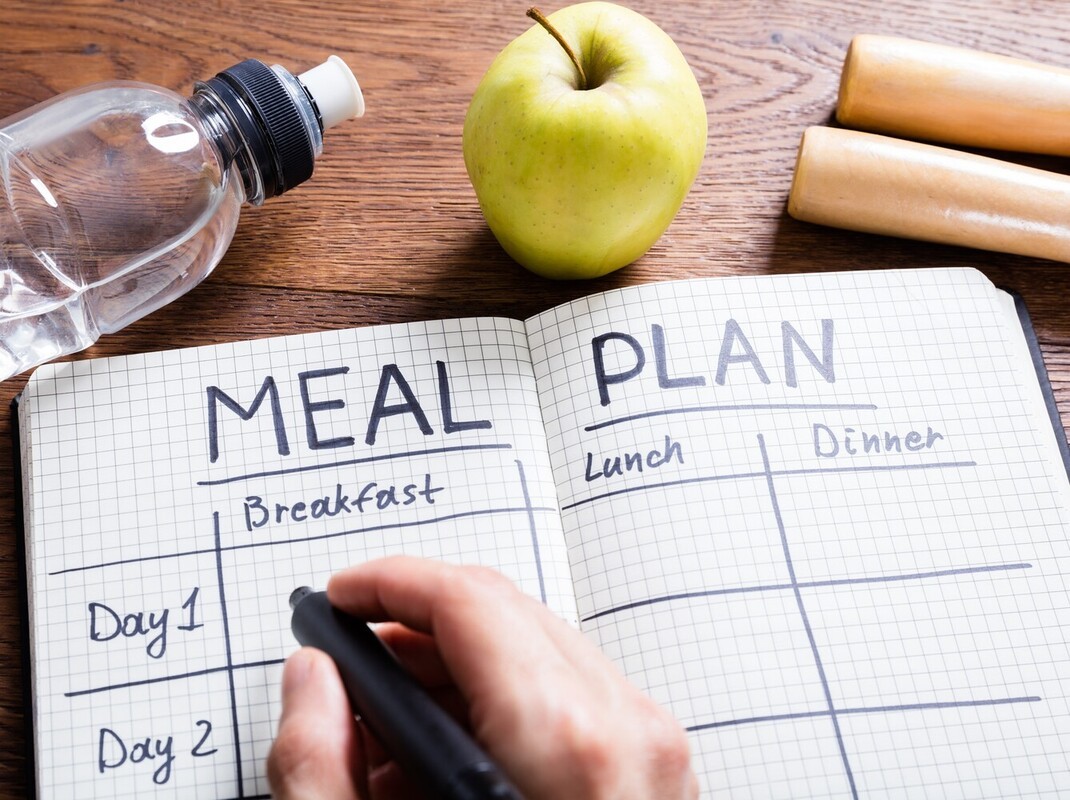 person writing a meal plan in their notebook while they learn how to walk and lose weight